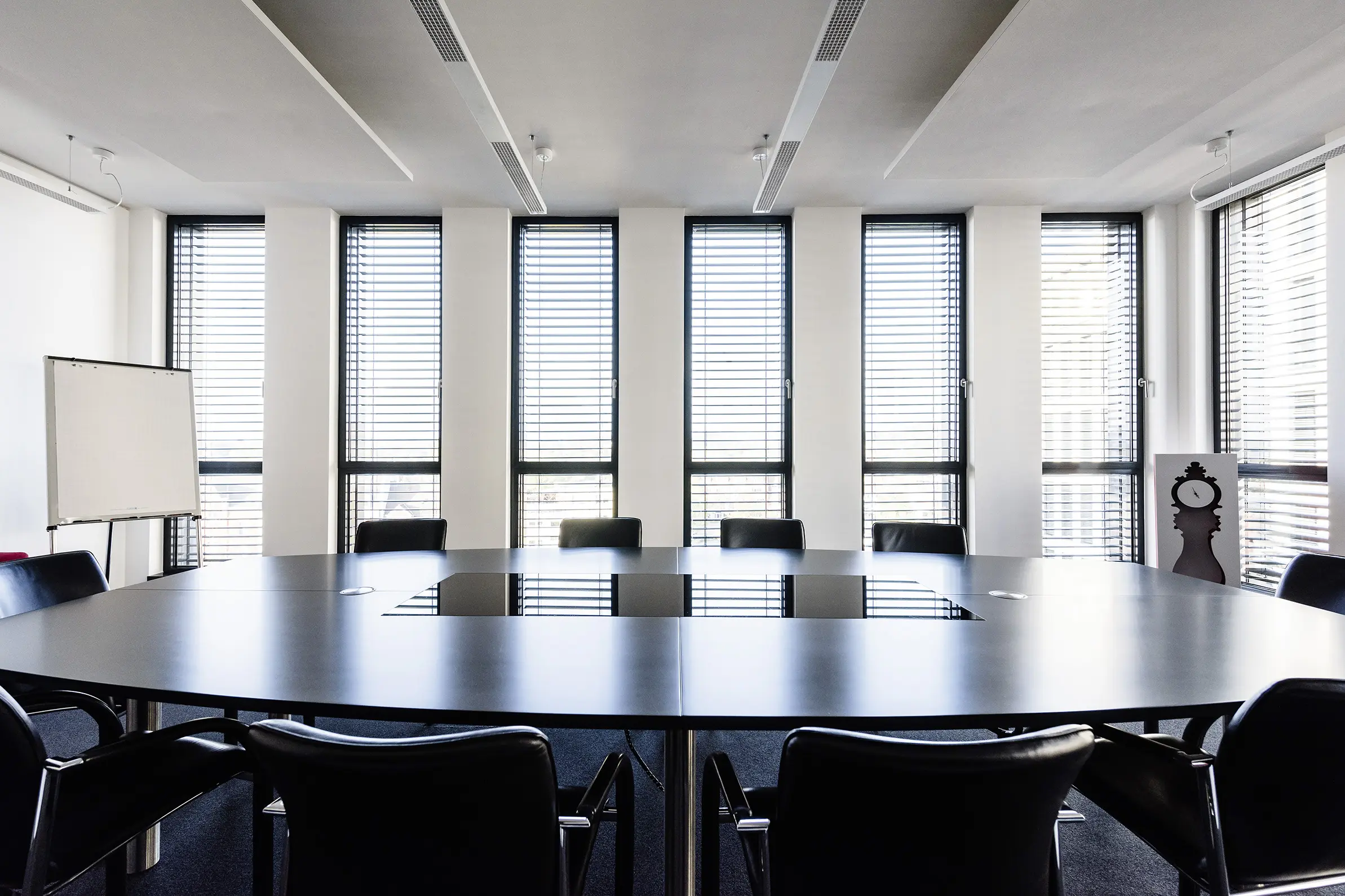 Moderner Konferenzraum mit großem schwarzem Besprechungstisch, schwarzen Lederstühlen und bodentiefen Fenstern mit Jalousien