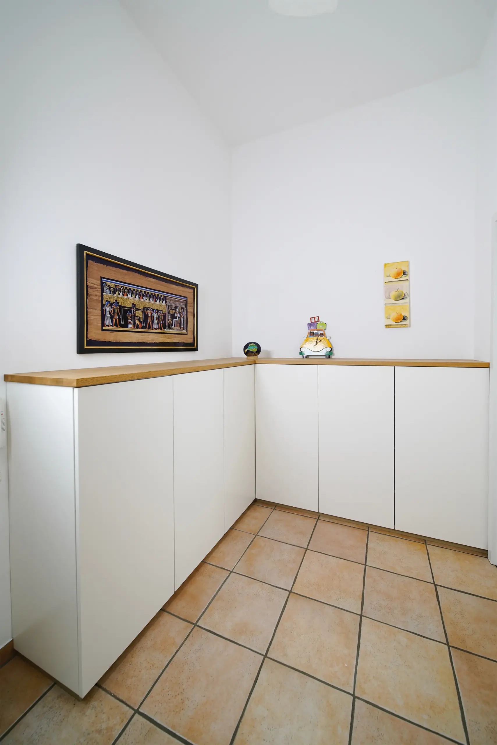 Maßgefertigtes weißes Eck-Sideboard mit Eichenholz-Abdeckplatte in einem hellen Raum mit Fliesenboden