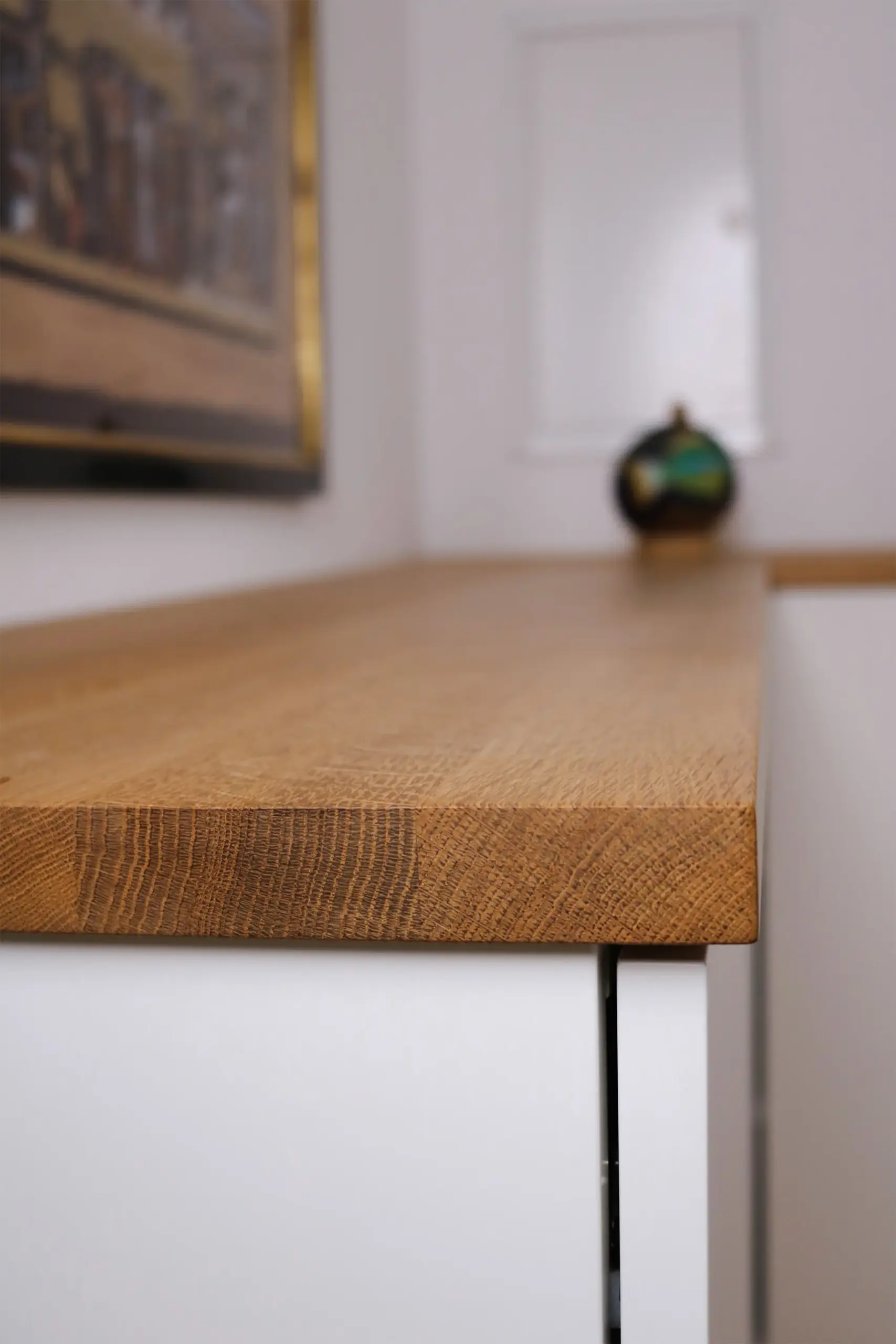 Nahaufnahme der abgerundeten Kante einer Eichenholz-Abdeckplatte auf einem weißen Sideboard