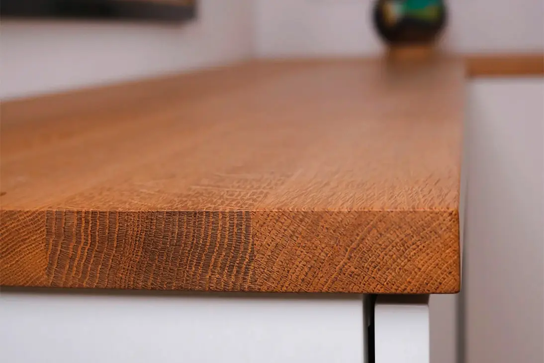 Nahaufnahme der abgerundeten Kante einer Eichenholz-Abdeckplatte auf einem weißen Sideboard