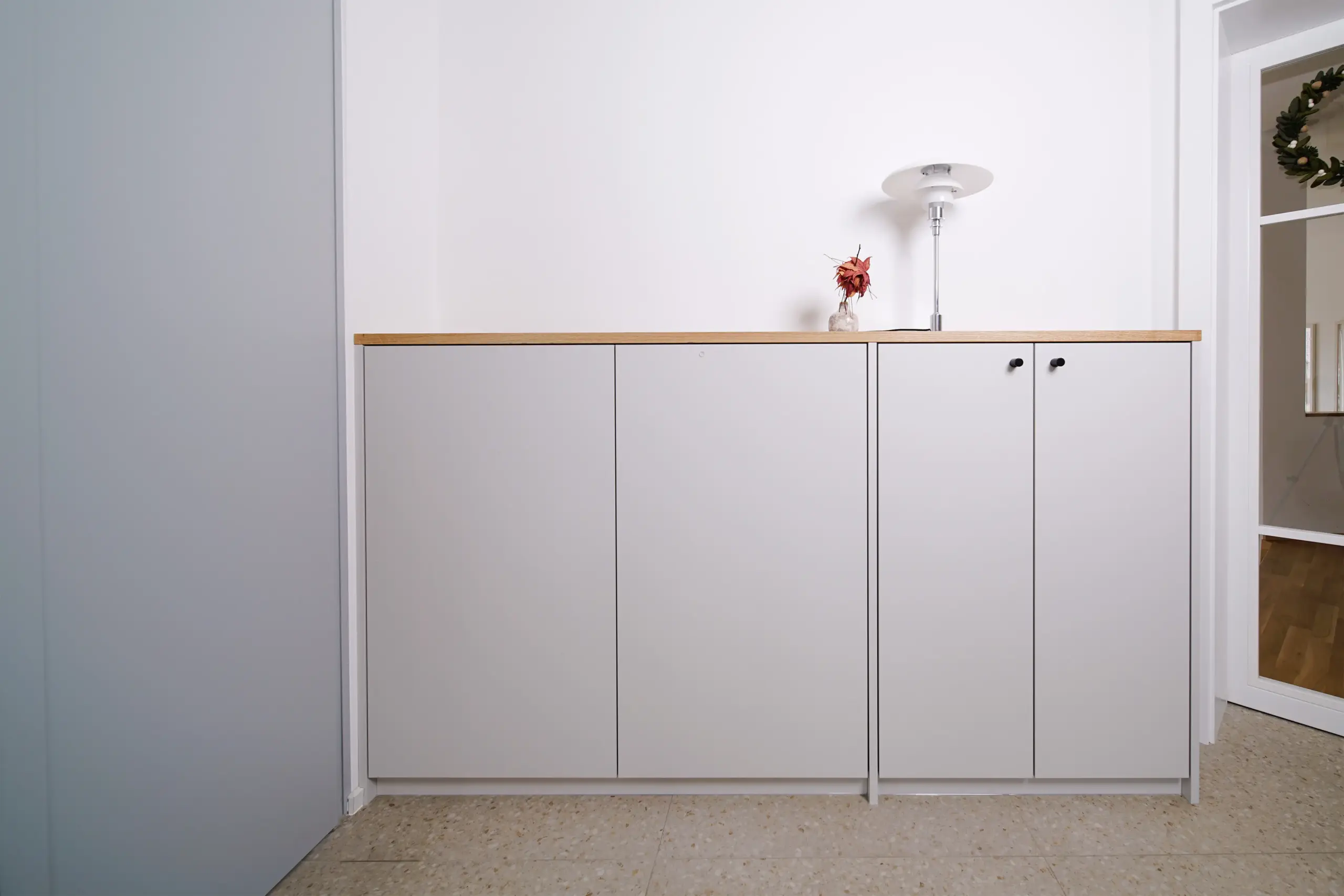 Maßgefertigtes weißes Sideboard mit Holzabdeckung und schlichten Fronten in einem hellen Wohnbereich