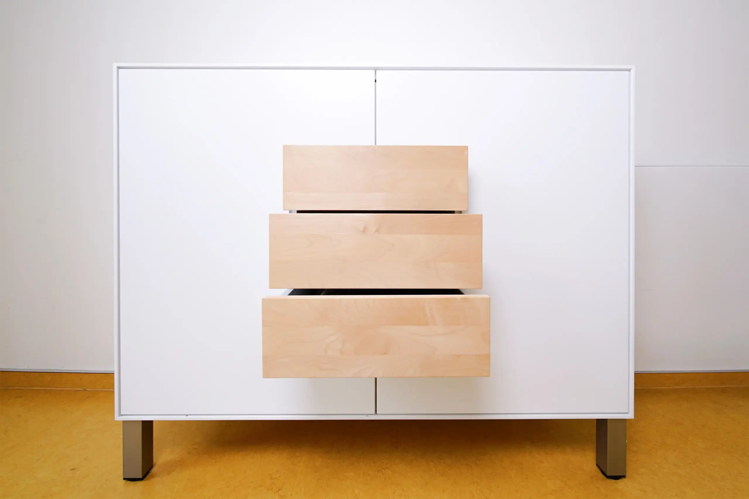 Weißes Highboard mit geöffneten Schubladen aus hellem Holz und schlanken Metallfüßen
