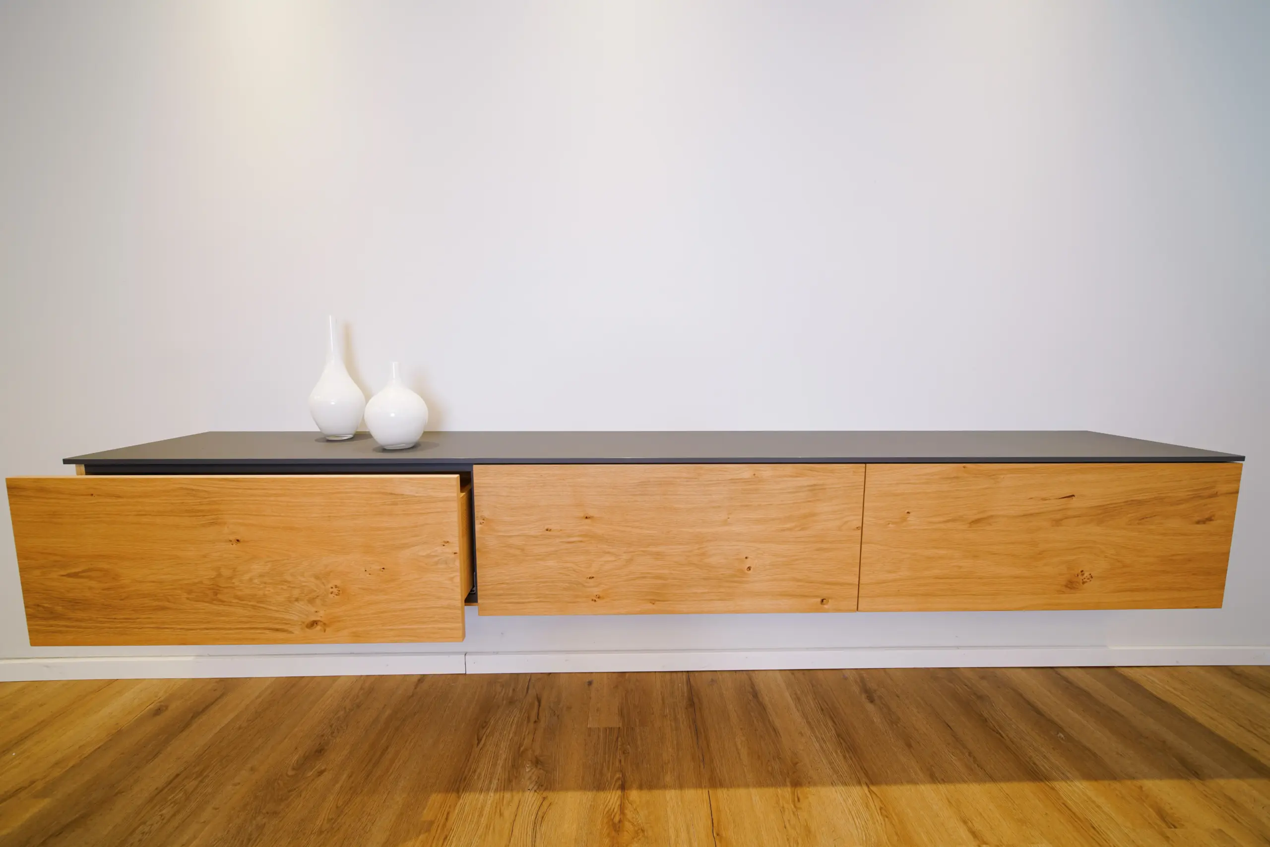 Wandmontiertes Holz-Sideboard mit geöffneter Schublade und dunkler Abdeckplatte