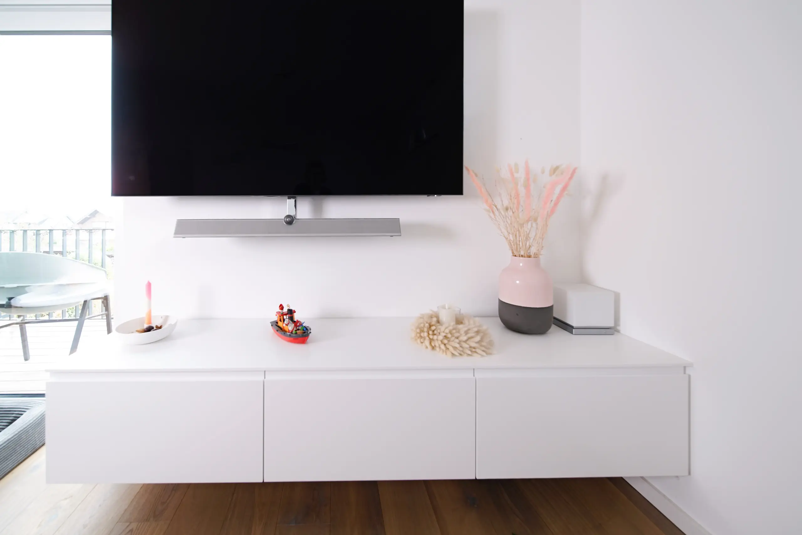 Minimalistisches weißes TV-Sideboard unter einem wandmontierten Fernseher in einem hellen Wohnbereich