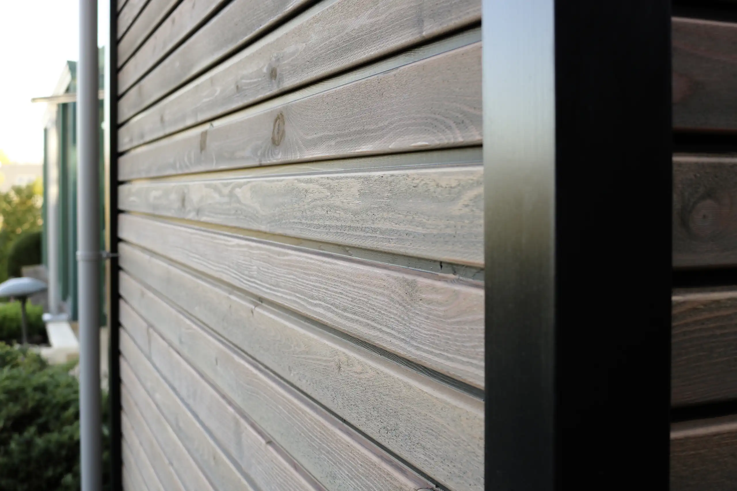 Detailaufnahme einer grau lasierten Holzfassade mit horizontalen Brettern und schwarzem Pfosten