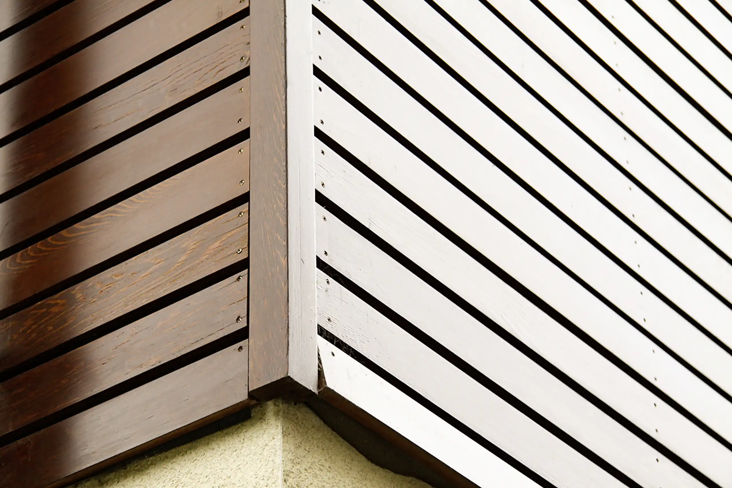 Detailansicht einer Hausecke mit dunkel lasierter und weiß gestrichener Holzfassade aus horizontalen Latten