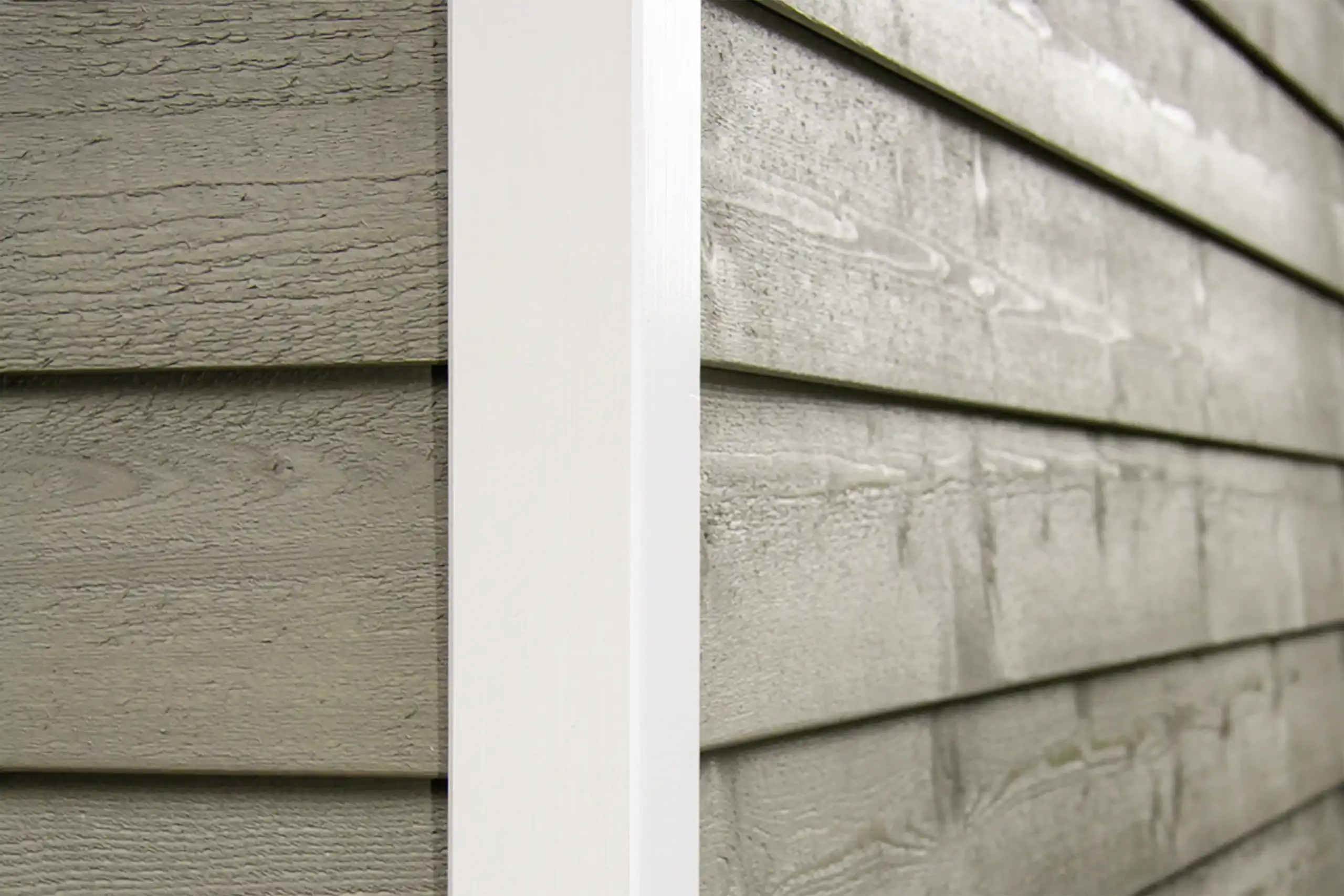Nahaufnahme der grau lasierten Holzverschalung einer modernen Gartenhütte mit weißer Eckleiste