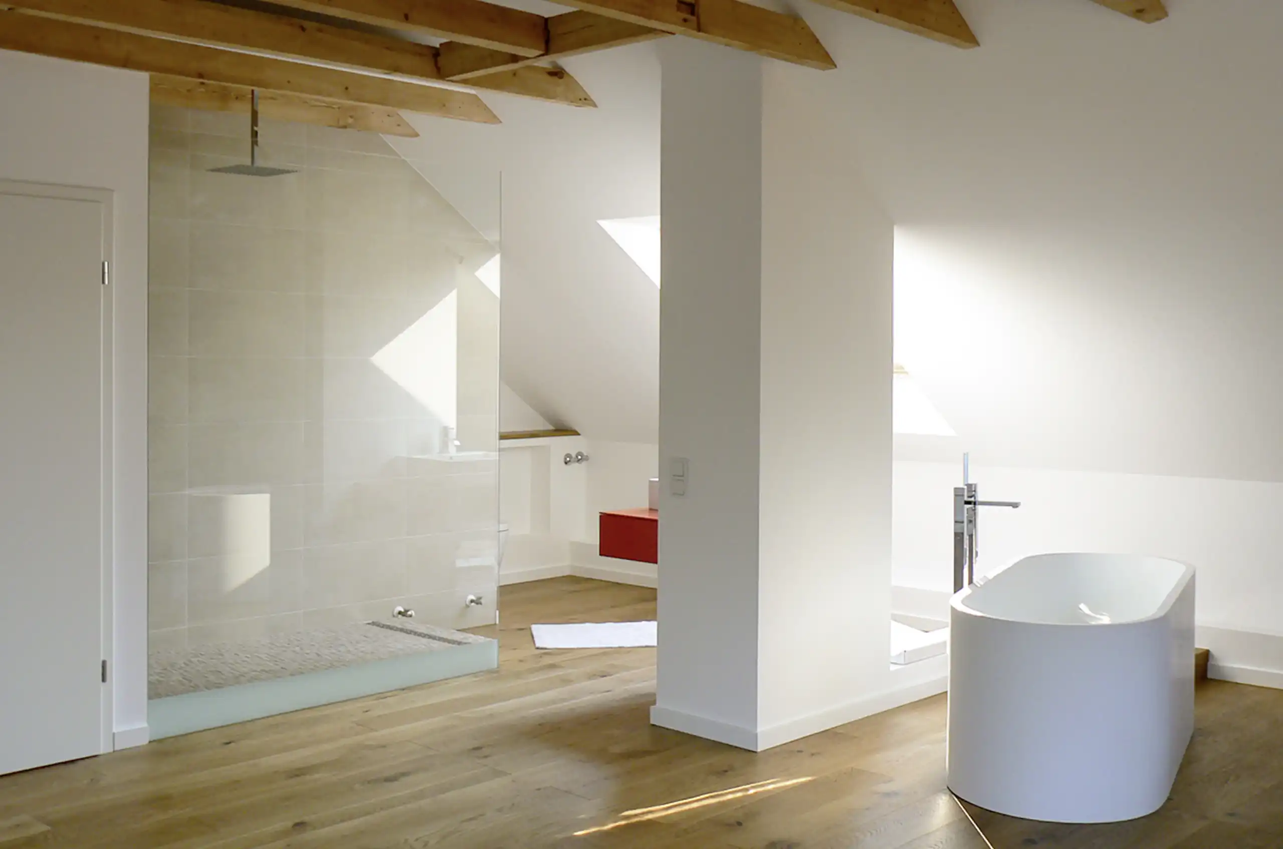 Helles Dachbad mit sichtbaren Holzbalken, bodengleicher Glasdusche, freistehender Badewanne und Eichenboden