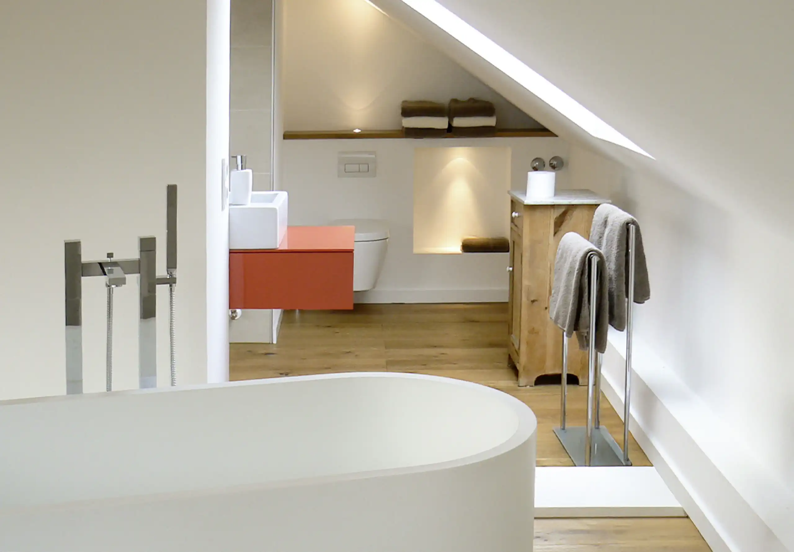 Modernes Badezimmer unter Dachschräge mit freistehender Badewanne, rotem Waschtischunterschrank, Holzmöbeln und Eichenboden