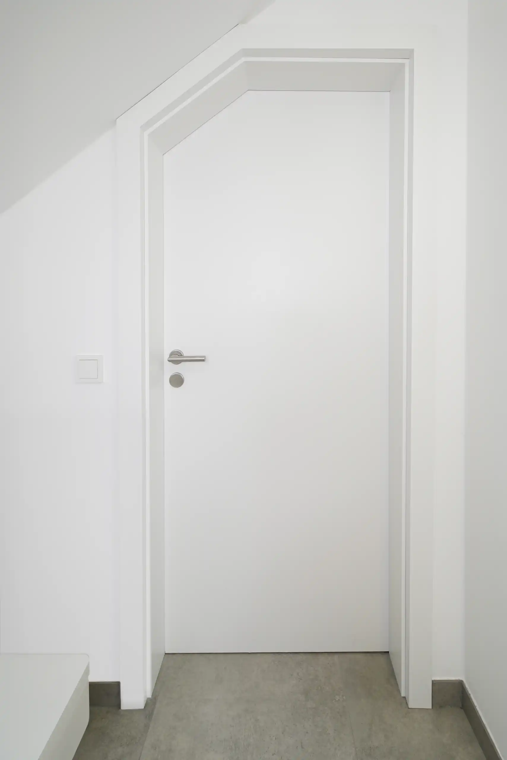 Weiße Innentür mit schlichtem Rahmen und Edelstahlklinke unter einer Dachschräge.