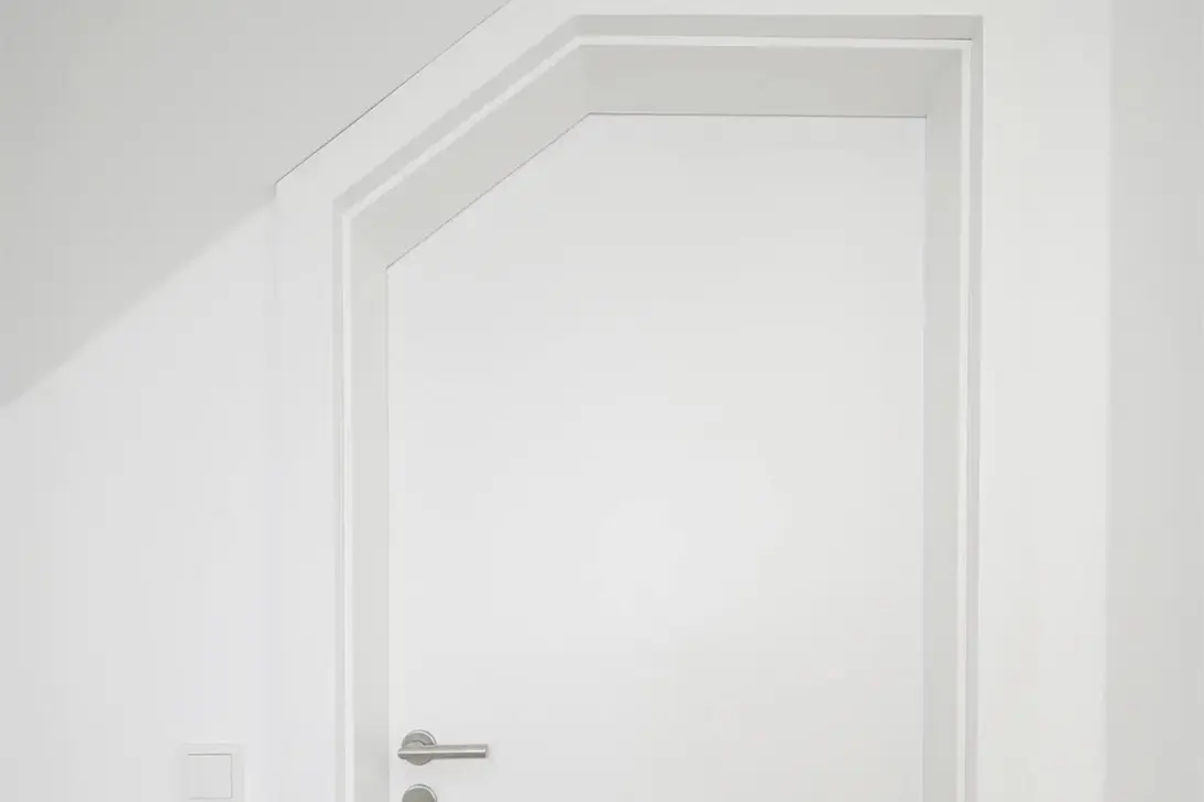 Weiße Innentür mit schlichtem Rahmen und Edelstahlklinke unter einer Dachschräge