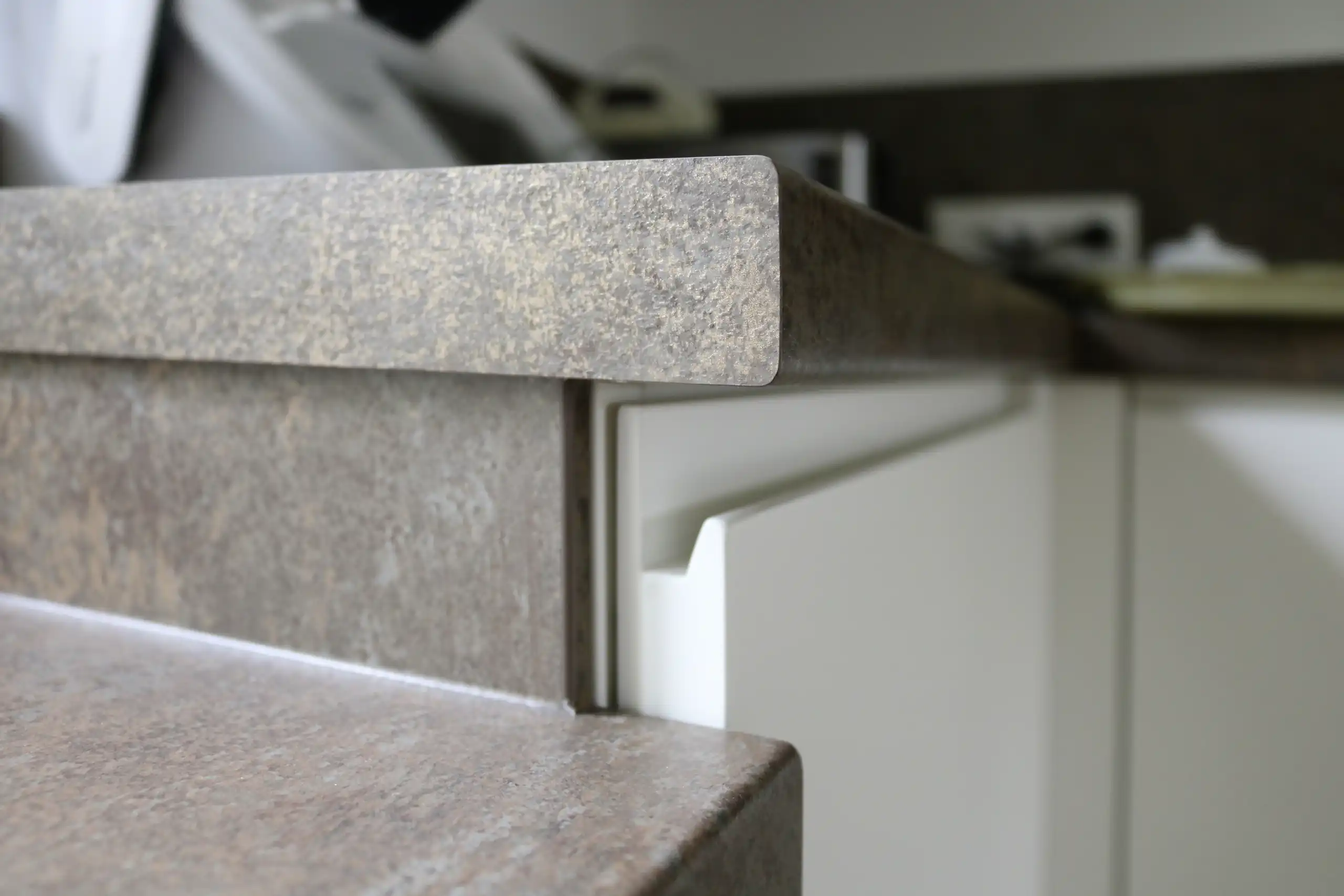 Detailaufnahme der robusten, dunkelgrauen Arbeitsplatte mit abgerundeter Kante und weißer Küchenfront
