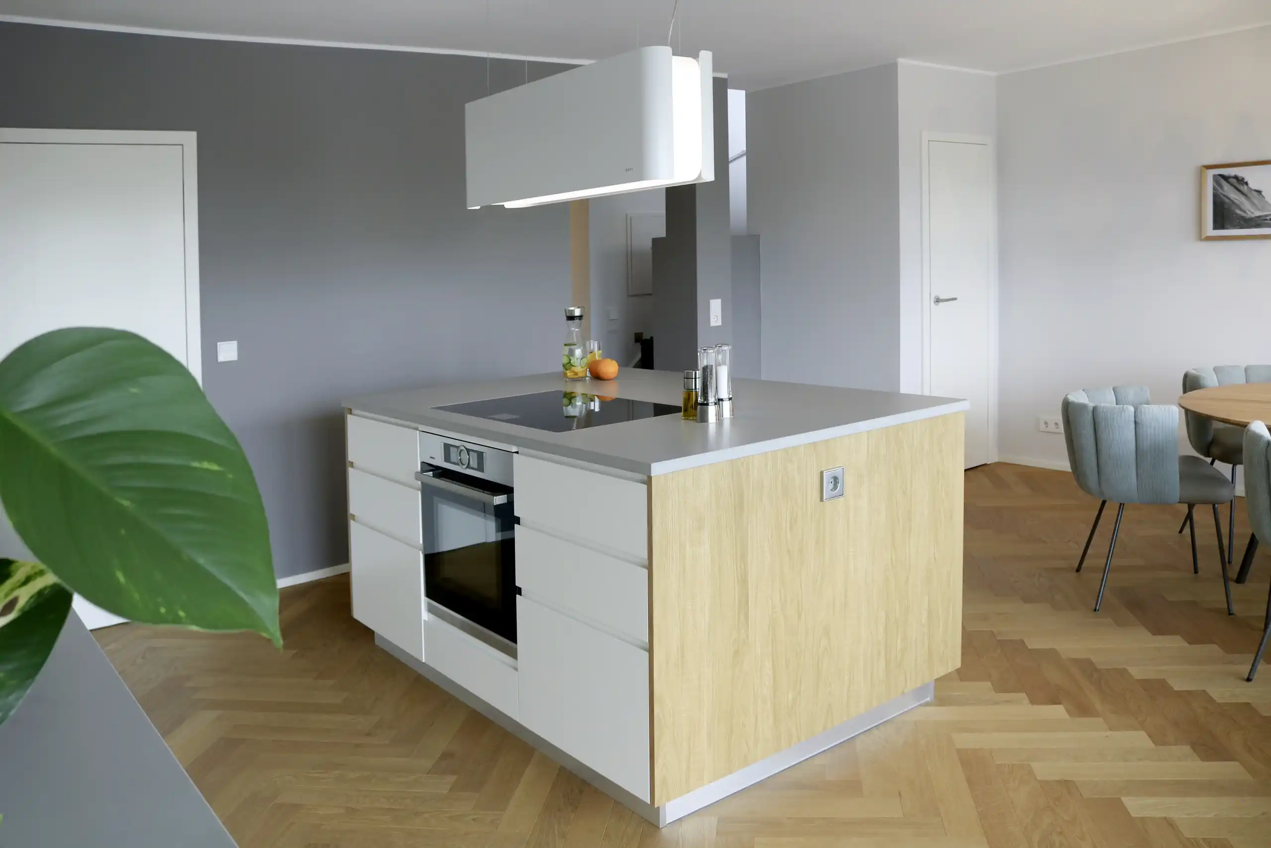 Nachgedacht für eine Sekunde Moderne Küche mit großer Kochinsel in Weiß und heller Holzoptik, integriertem Backofen, Induktionskochfeld und schwebender Dunstabzugshaube im offenen Wohnbereich
