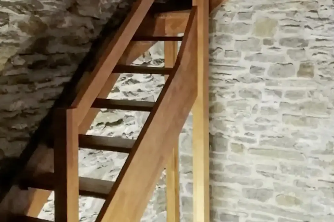 Raumsparende Holztreppe mit offenen Stufen und schlichtem Geländer vor rustikalen Natursteinwänden