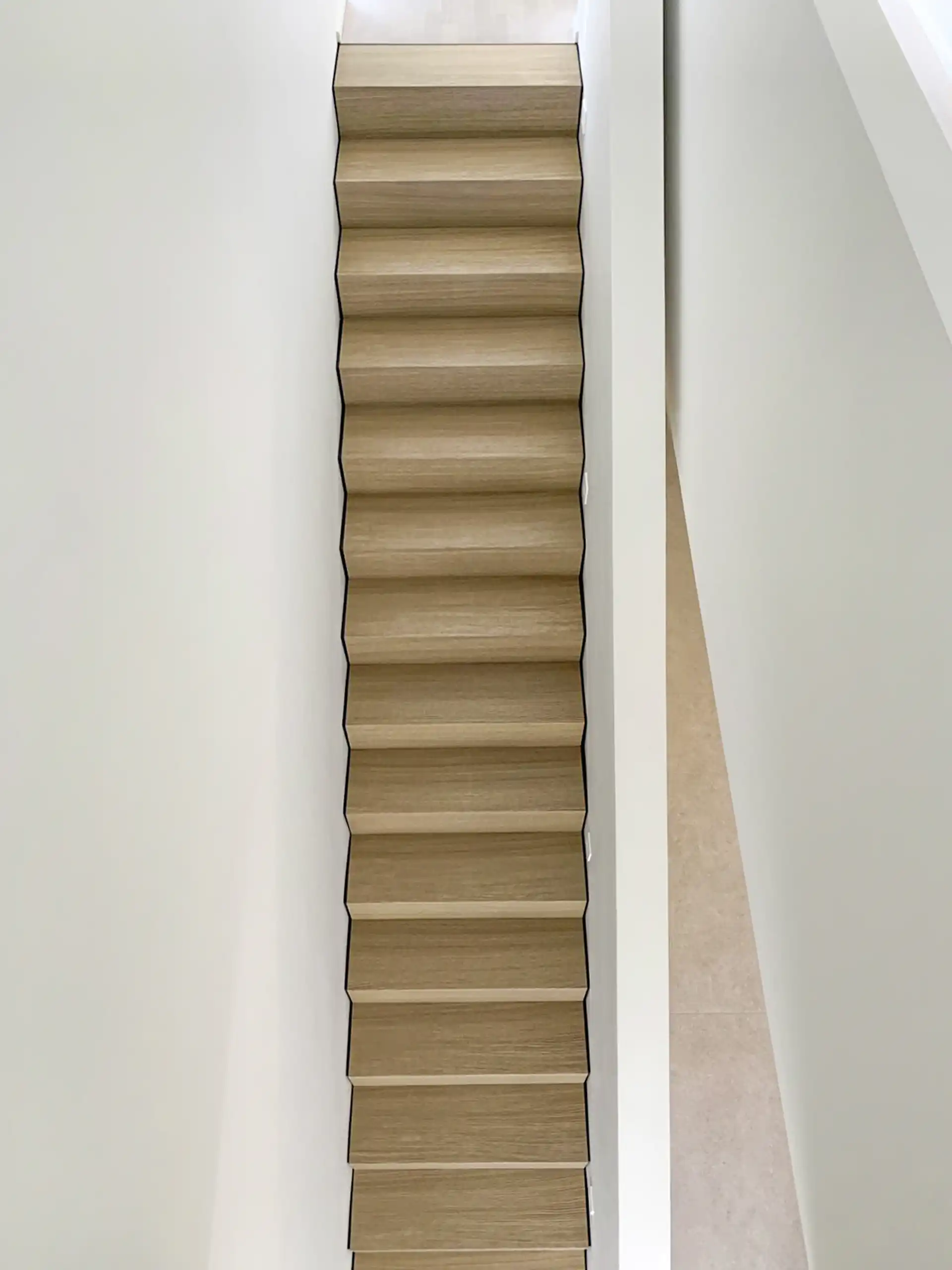 Schmale Holztreppe mit durchgehender Schattenfuge zwischen den hellen Eichenstufen und den weißen Wänden