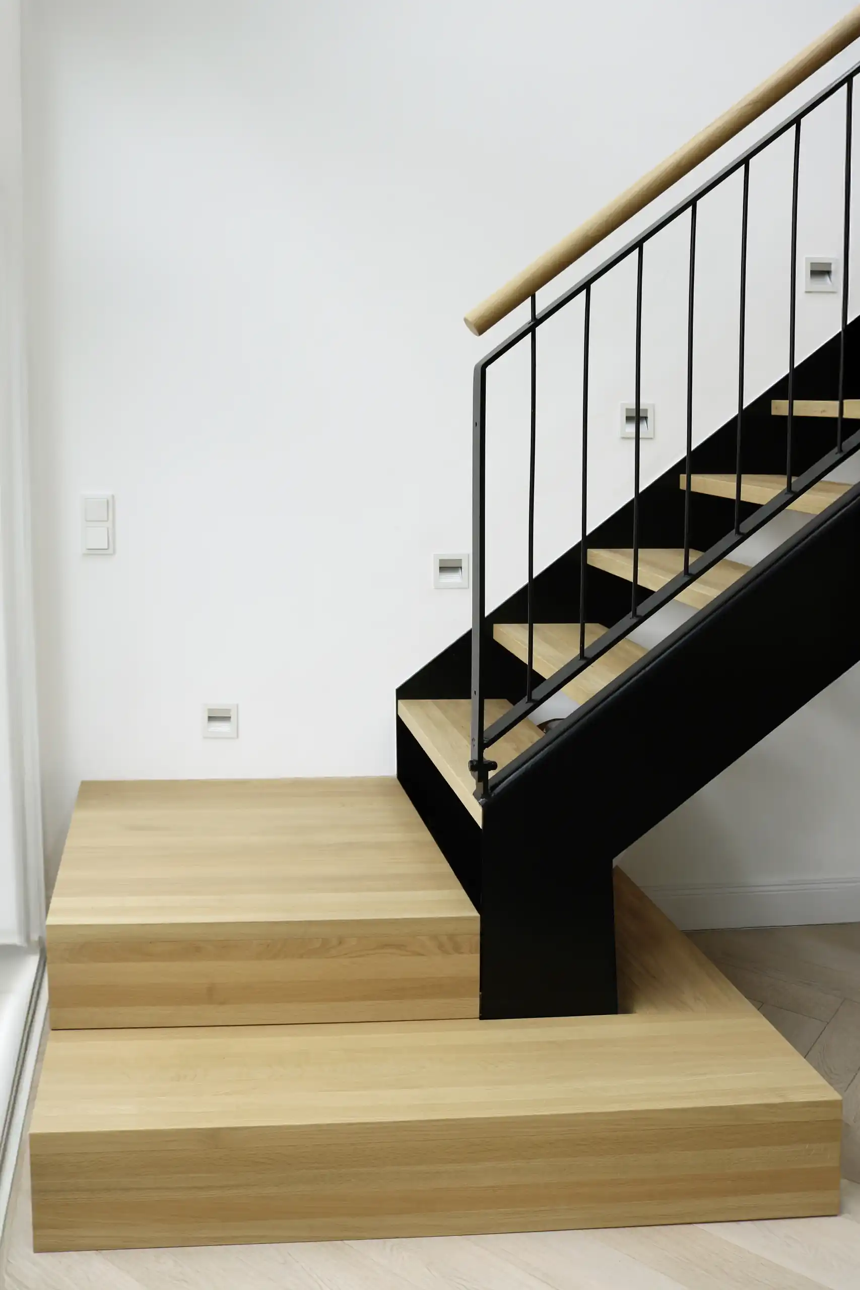 Moderne Treppe mit massiven Holzstufen, schwarzer Stahlwange und filigranem Metallgeländer mit Holzhandlauf
