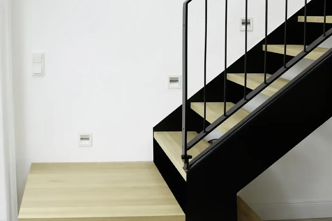 Moderne Treppe mit massiven Holzstufen, schwarzer Stahlwange und filigranem Metallgeländer mit Holzhandlauf