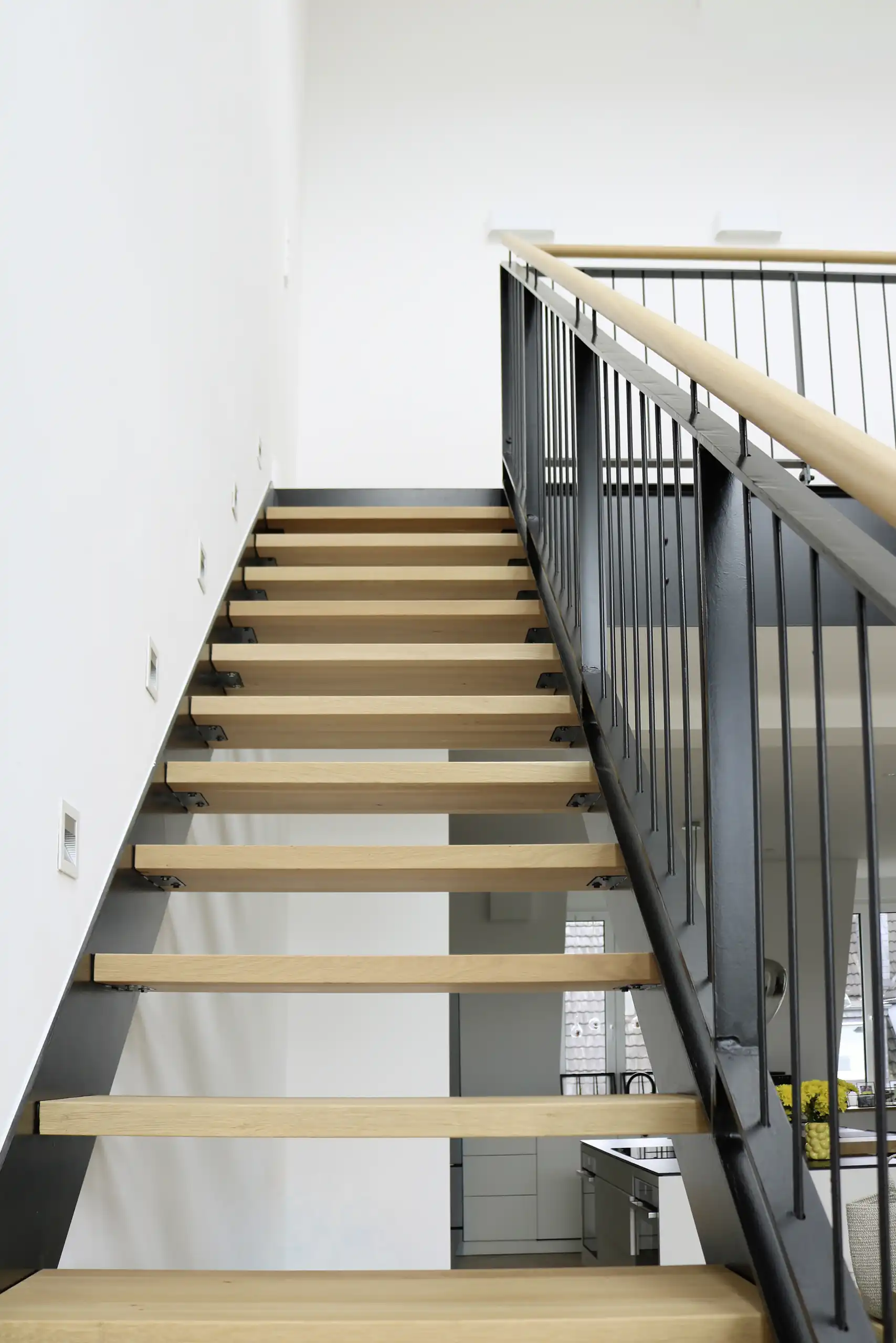 Moderne Treppe mit massiven Holzstufen, schwarzer Stahlwange und filigranem Metallgeländer mit Holzhandlauf