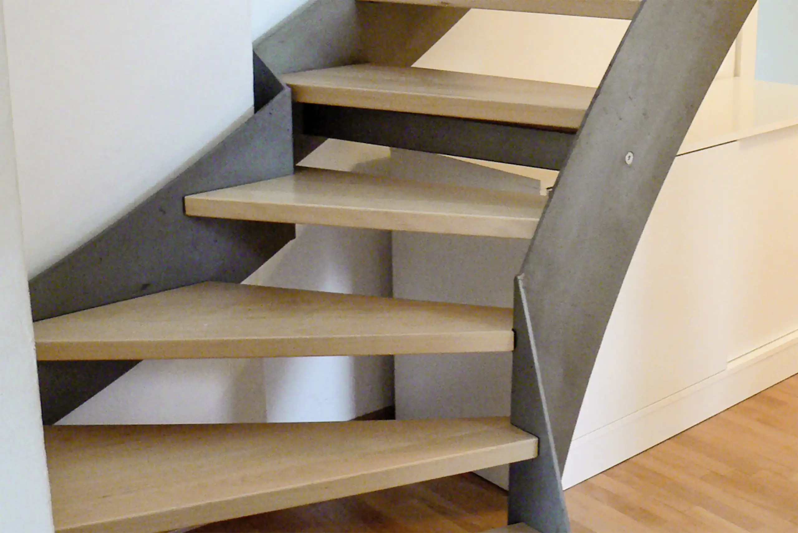 Offene Treppe mit hellen Holzstufen, dunklen Stahlwangen und geschwungenem Treppenverlauf