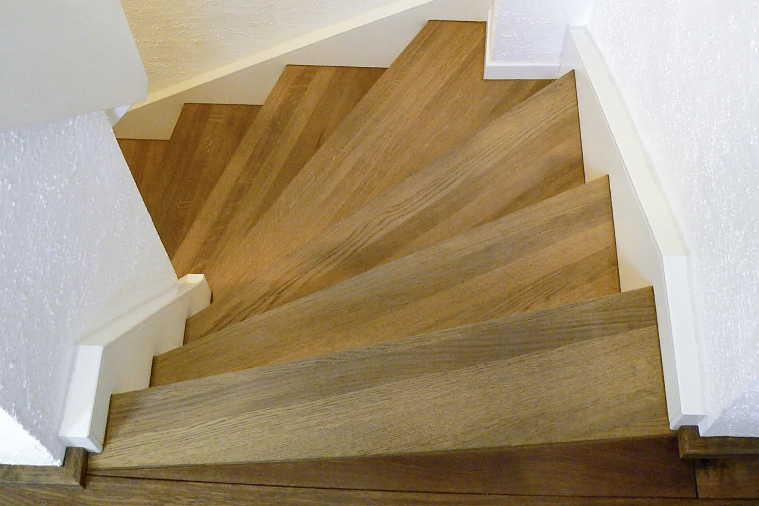 Blick von oben auf eine schmale Treppe mit gewendelten Eichenholzstufen und weißen Wandabschlüssen