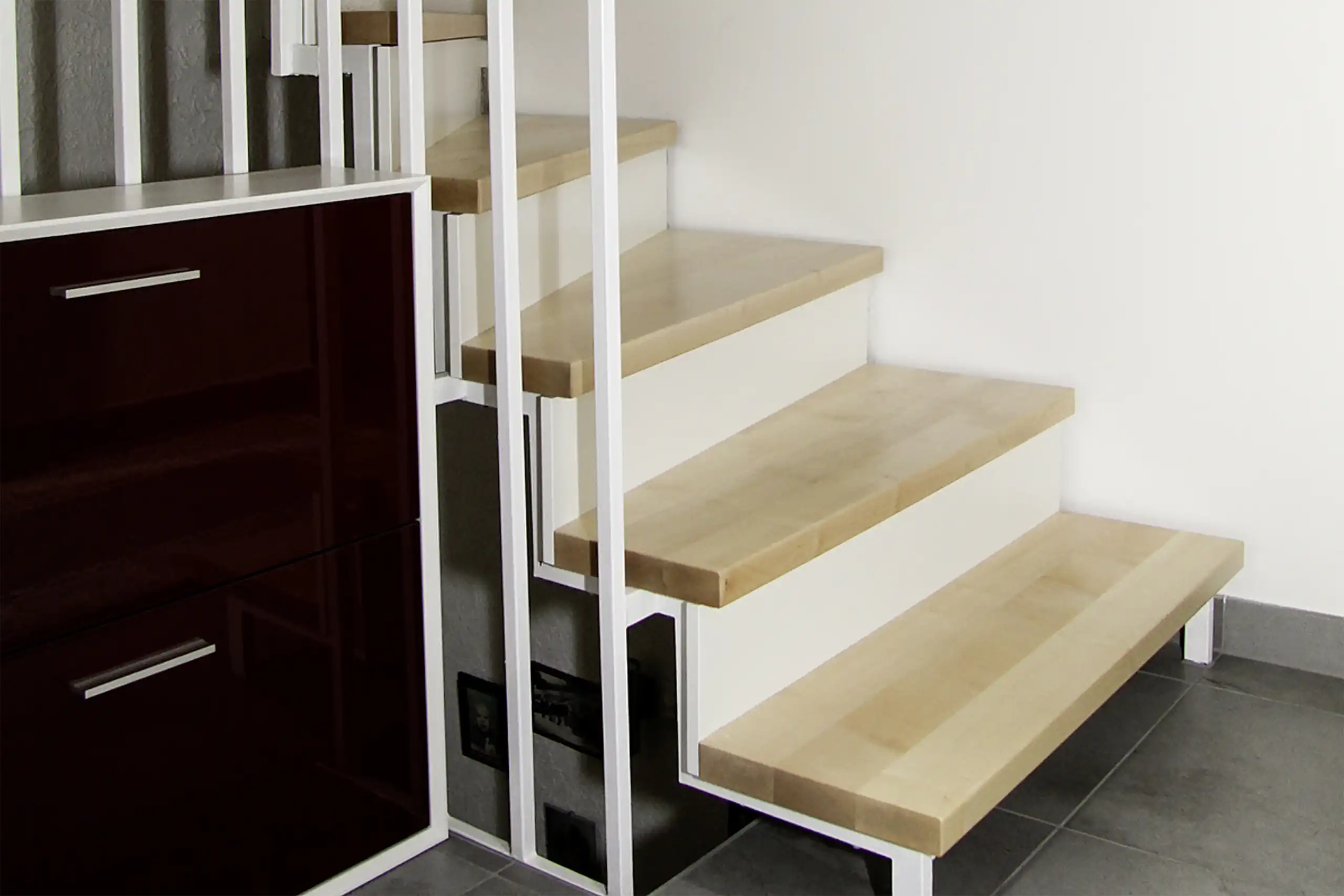 Renovierte Stahltreppe mit hellen Holzstufen, weißem Metallgeländer und dunkelbraunem Einbauschrank