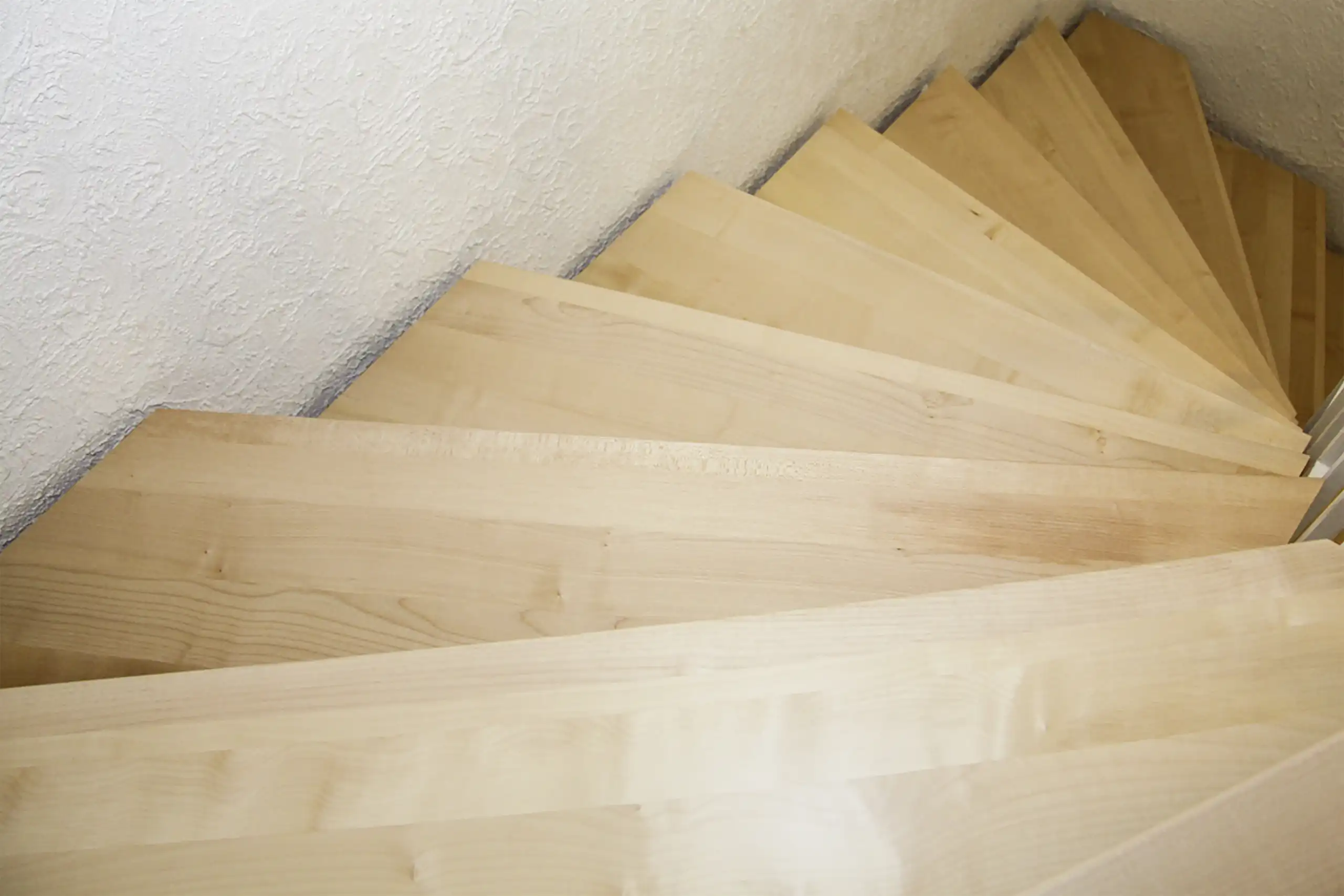 Wendeltreppe mit hellen Holzstufen in einem schmalen Treppenhaus mit weiß verputzten Wänden