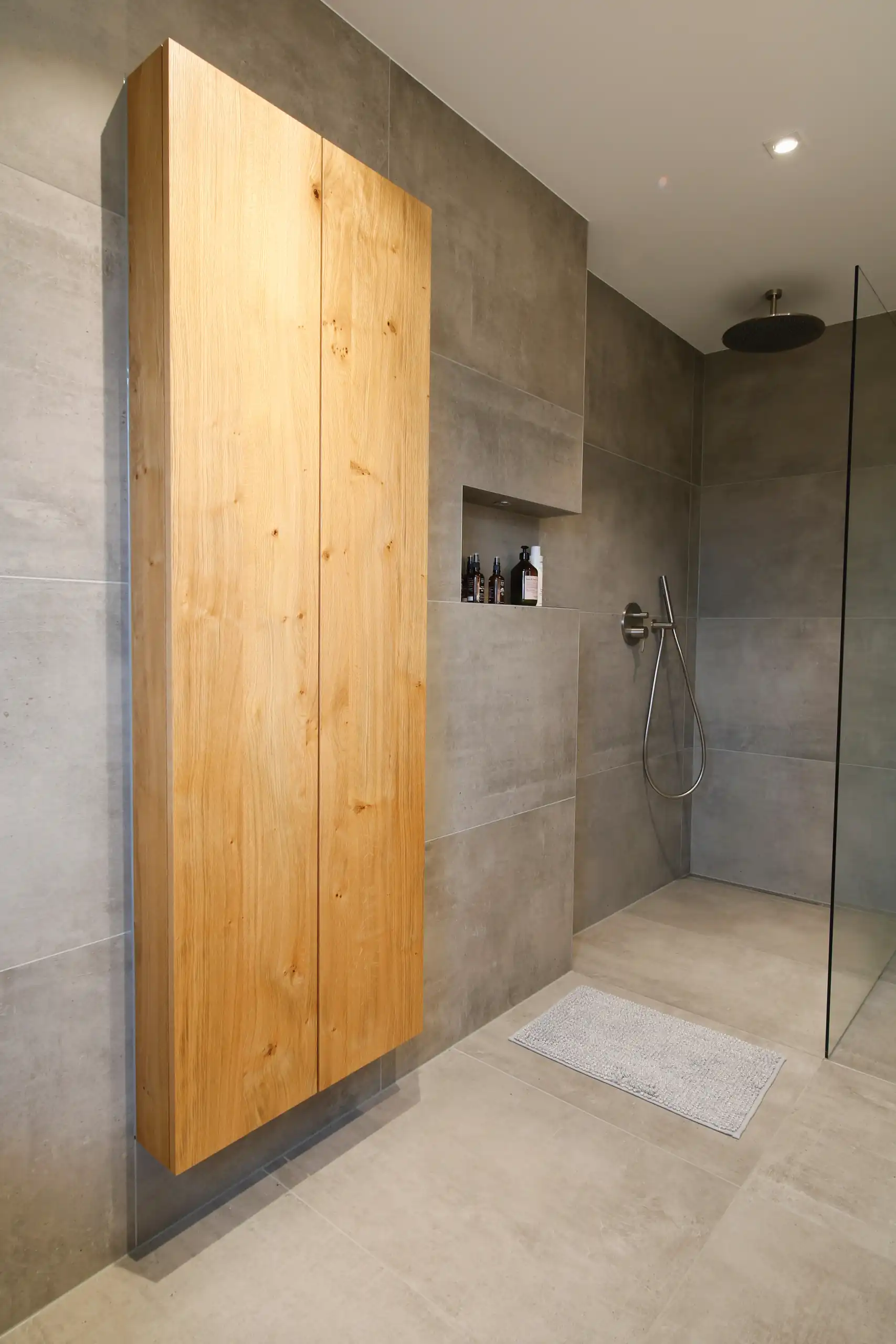Modernes Badezimmer mit großformatigen grauen Fliesen, bodengleicher Dusche mit Glaswand und einem hohen Einbauschrank aus Eiche