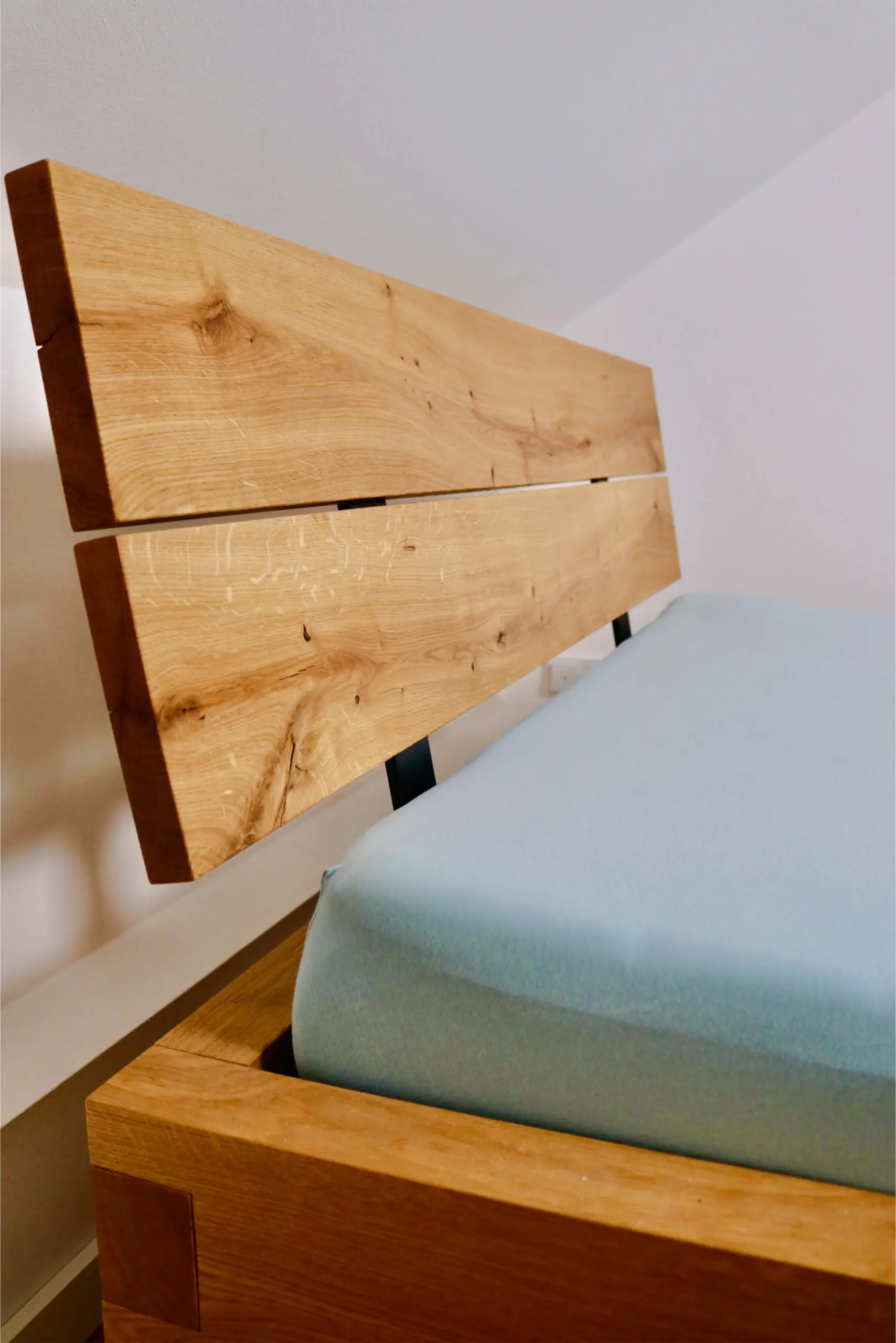 Seitenansicht des Eichenkopfteils und Bettrahmens mit hellblauer Matratze in einem hellen Schlafzimmer