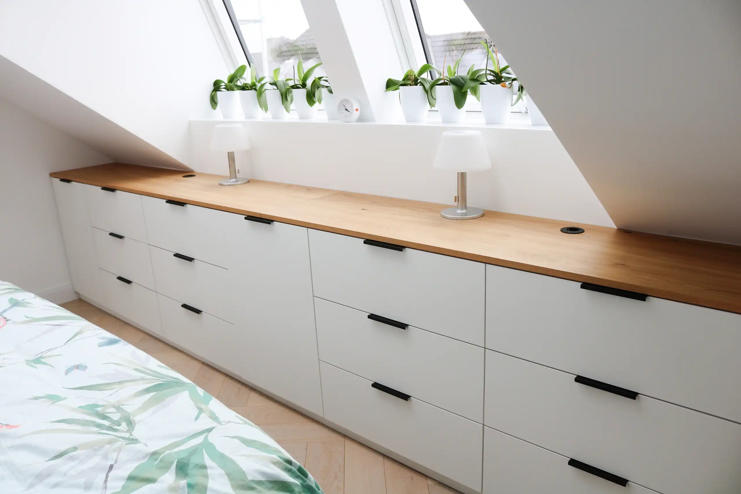 Maßgefertigter weißer Einbauschrank unter einer Dachschräge mit Holzabdeckung und schwarzen Griffen