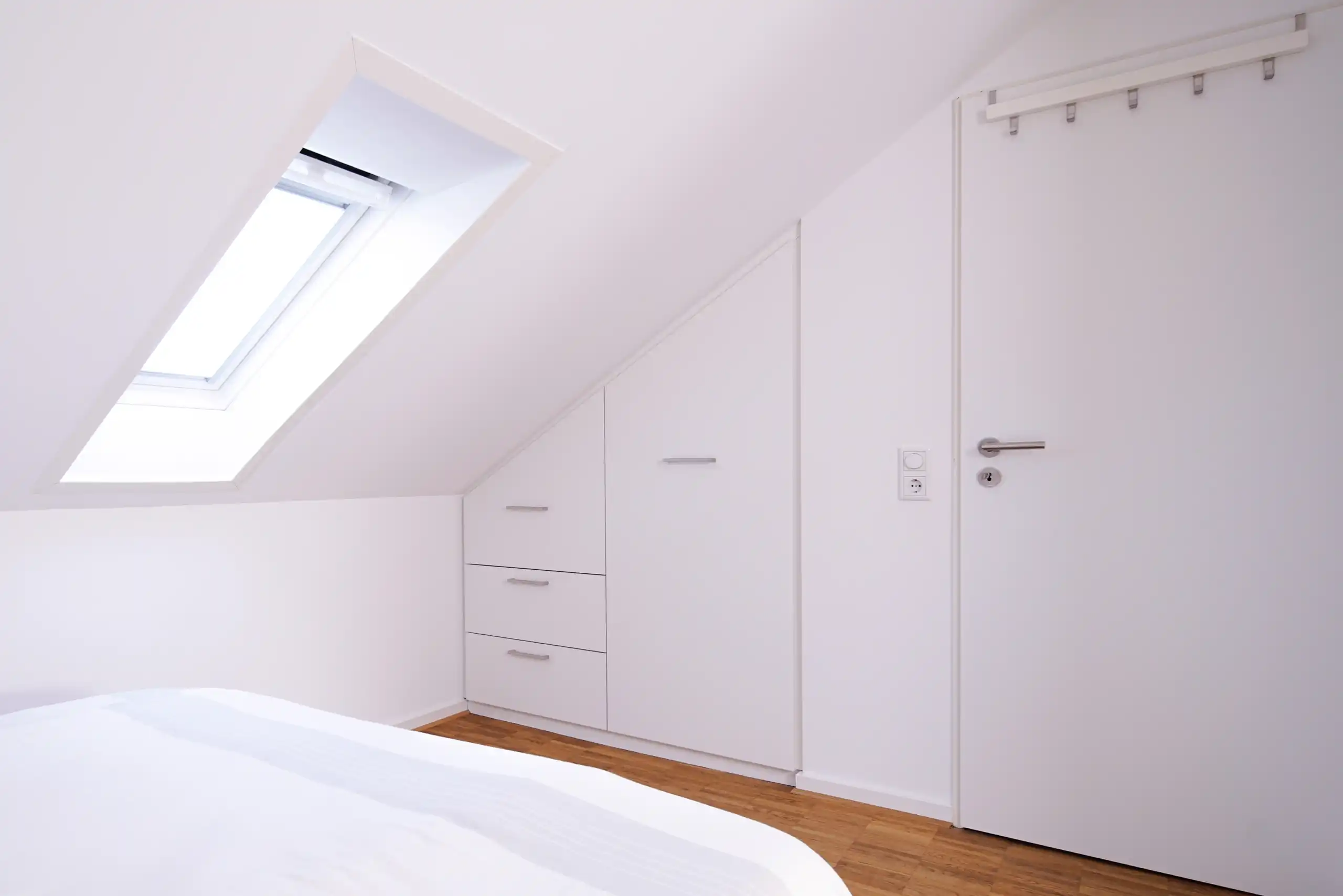 Individuelle weiße Einbaulösung unter der Dachschräge mit Schranktüren und Schubladen im Schlafzimmer