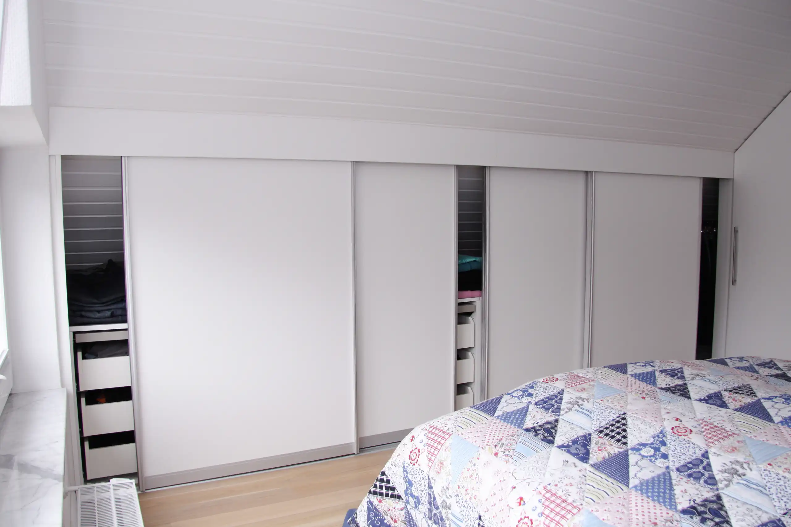 Weißer Drempelschrank mit Schiebetüren und integrierten Auszügen im Schlafzimmer unter der Dachschräge