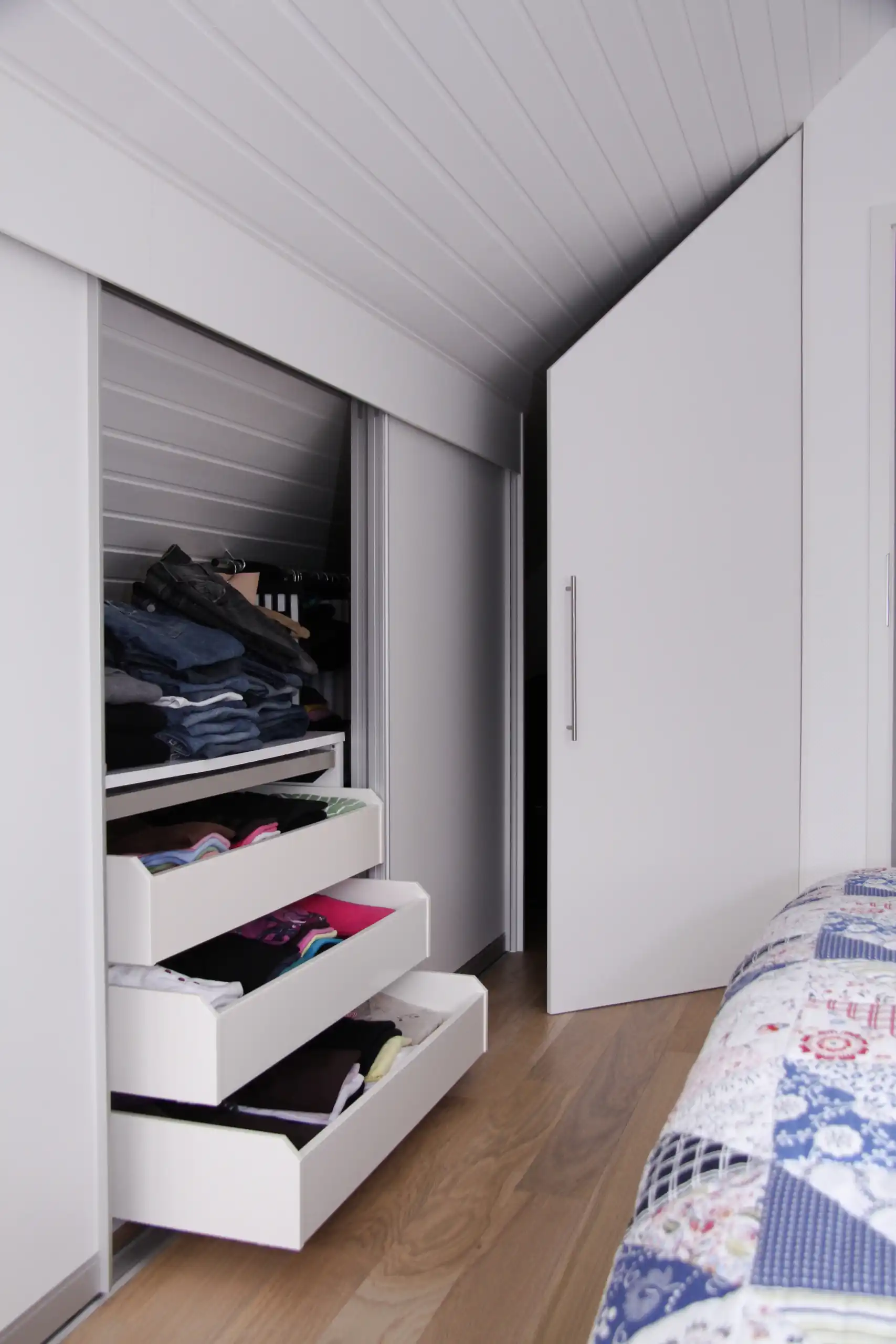 Geöffneter Drempelschrank mit Auszügen, Stauraum für Kleidung und passgenauer Anpassung an die Dachschräge