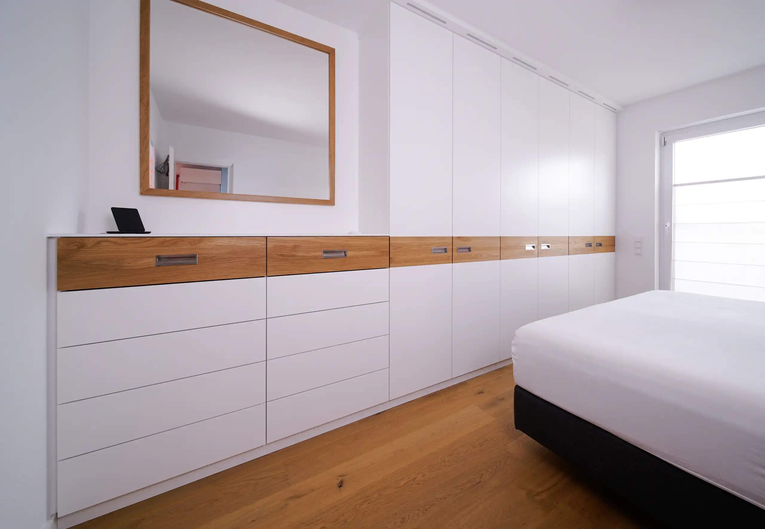 Individuelle Schrank- und Kommodenlösung mit weißen Fronten, Eichenholz-Akzenten und integriertem Stauraum im Schlafzimmer
