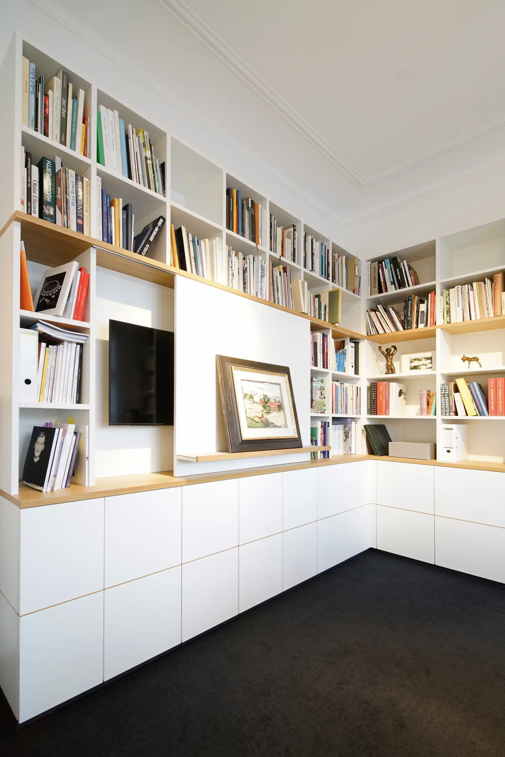 Weiße Einbaubibliothek mit offenen Bücherregalen, Holzablagen, integriertem TV-Fach und geschlossenen Unterschränken