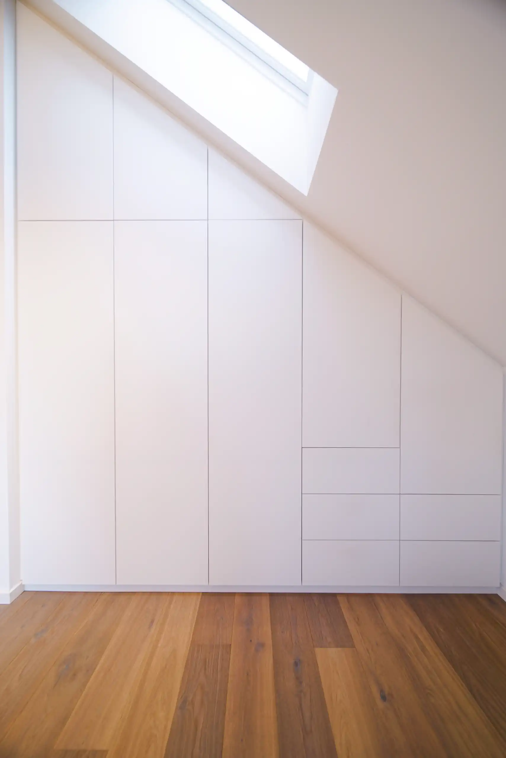 Maßgefertigter weißer Einbauschrank unter einer Dachschräge mit passgenauen Schranktüren und integrierten Schubladen