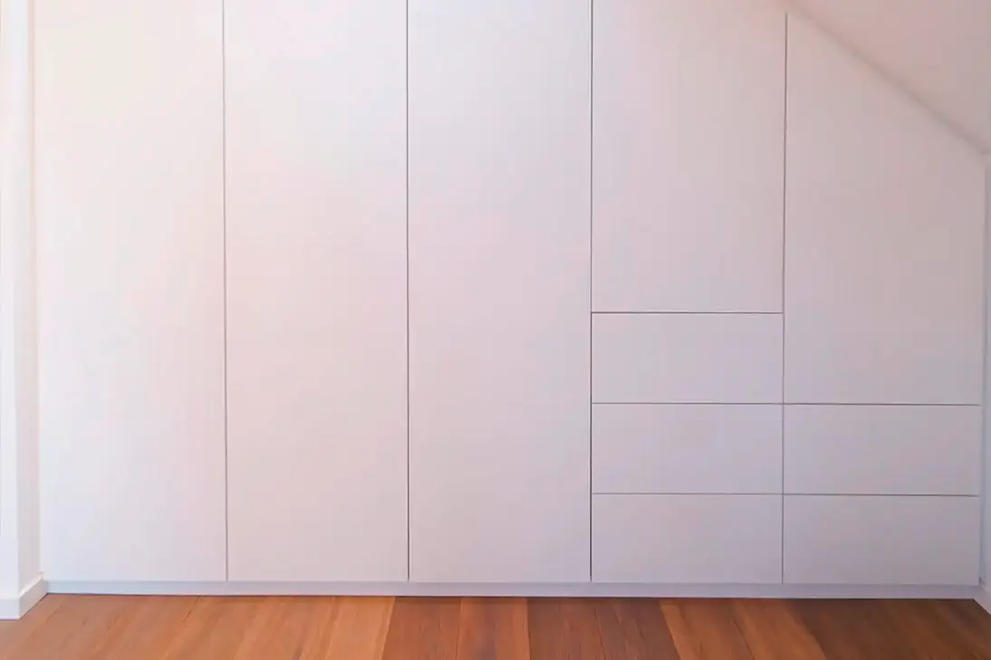 Maßgefertigter weißer Einbauschrank unter einer Dachschräge mit passgenauen Schranktüren und integrierten Schubladen