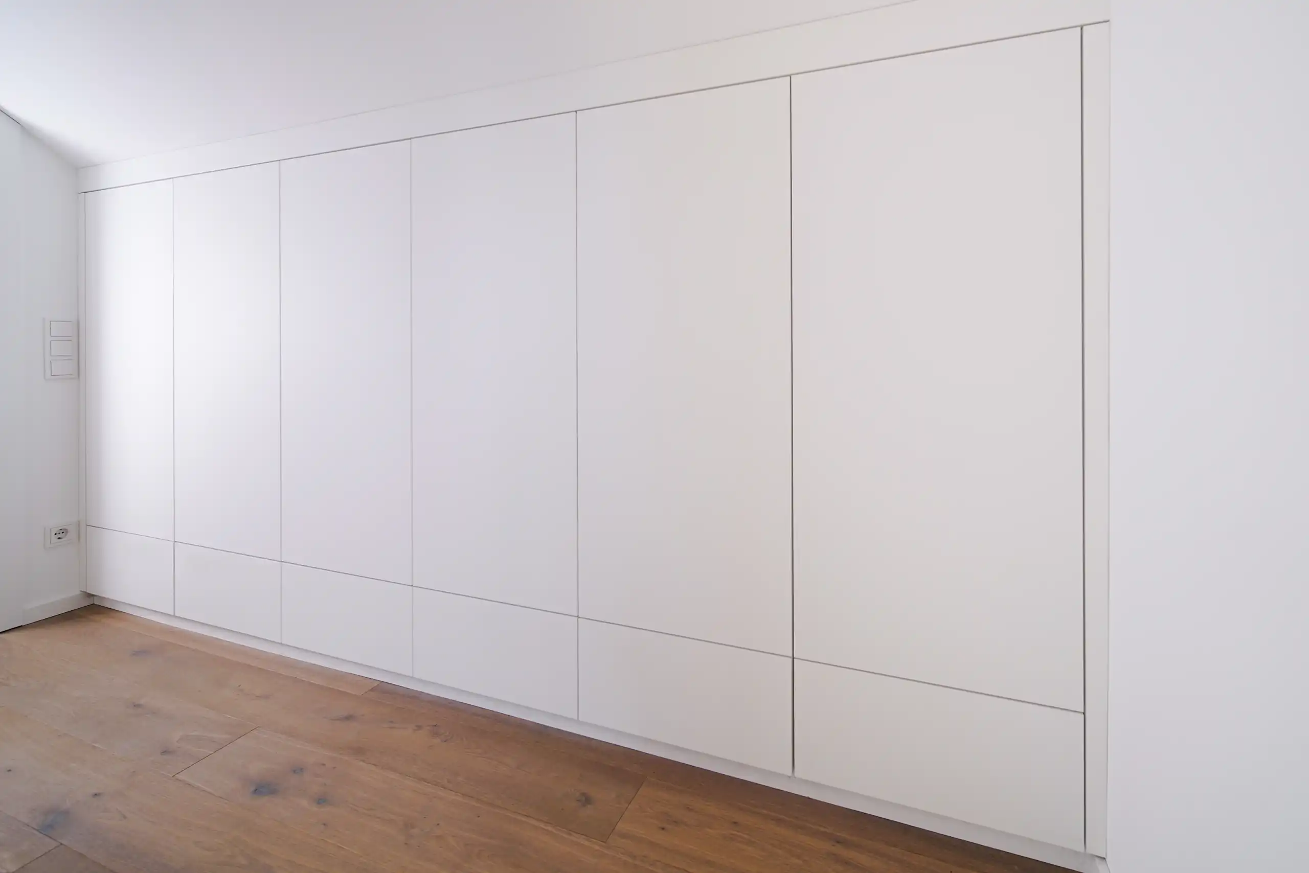 Maßgefertigter weißer Einbauschrank mit grifflosen Fronten, integrierten unteren Schubladen und passgenauer Anpassung an Wand und Decke