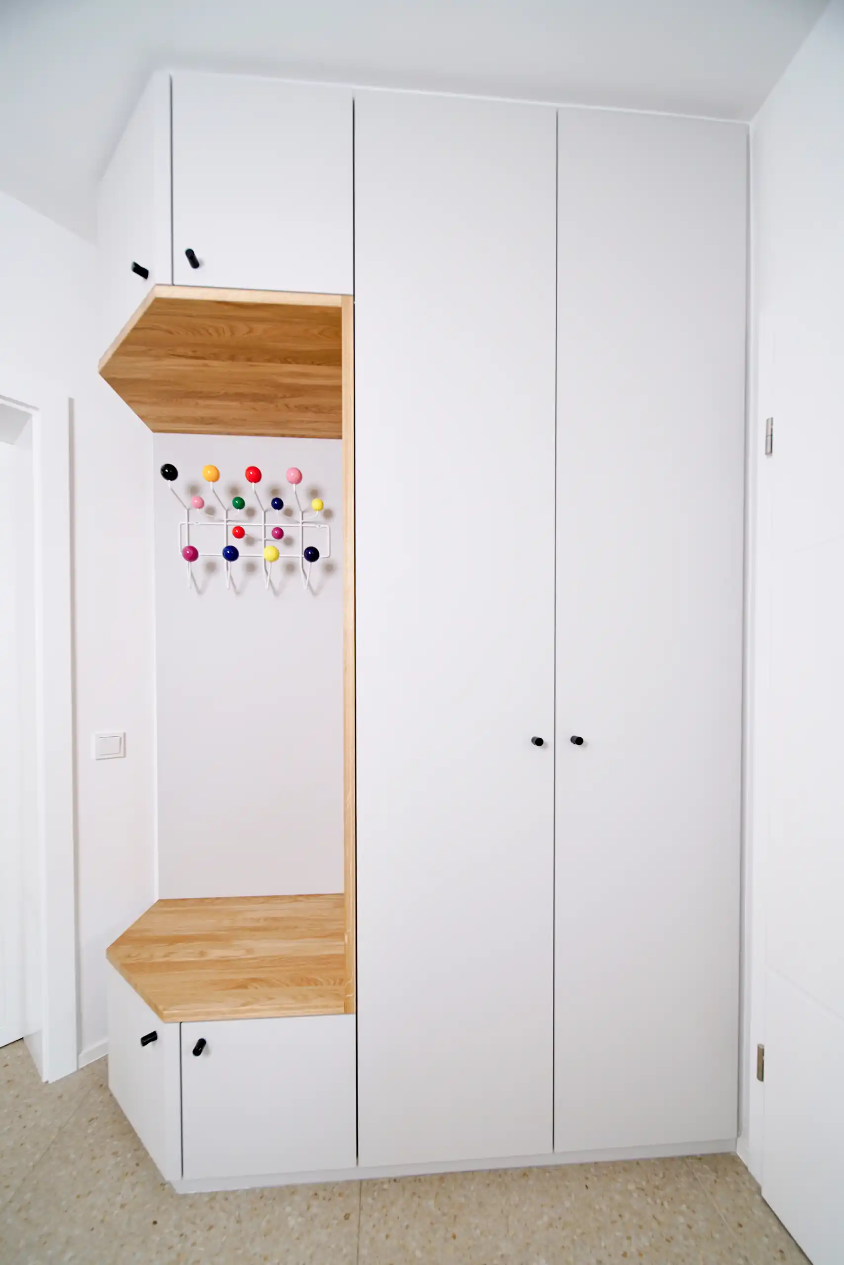 Weiße Einbaugarderobe mit deckenhohen Schranktüren und offener Sitznische aus Eichenholz