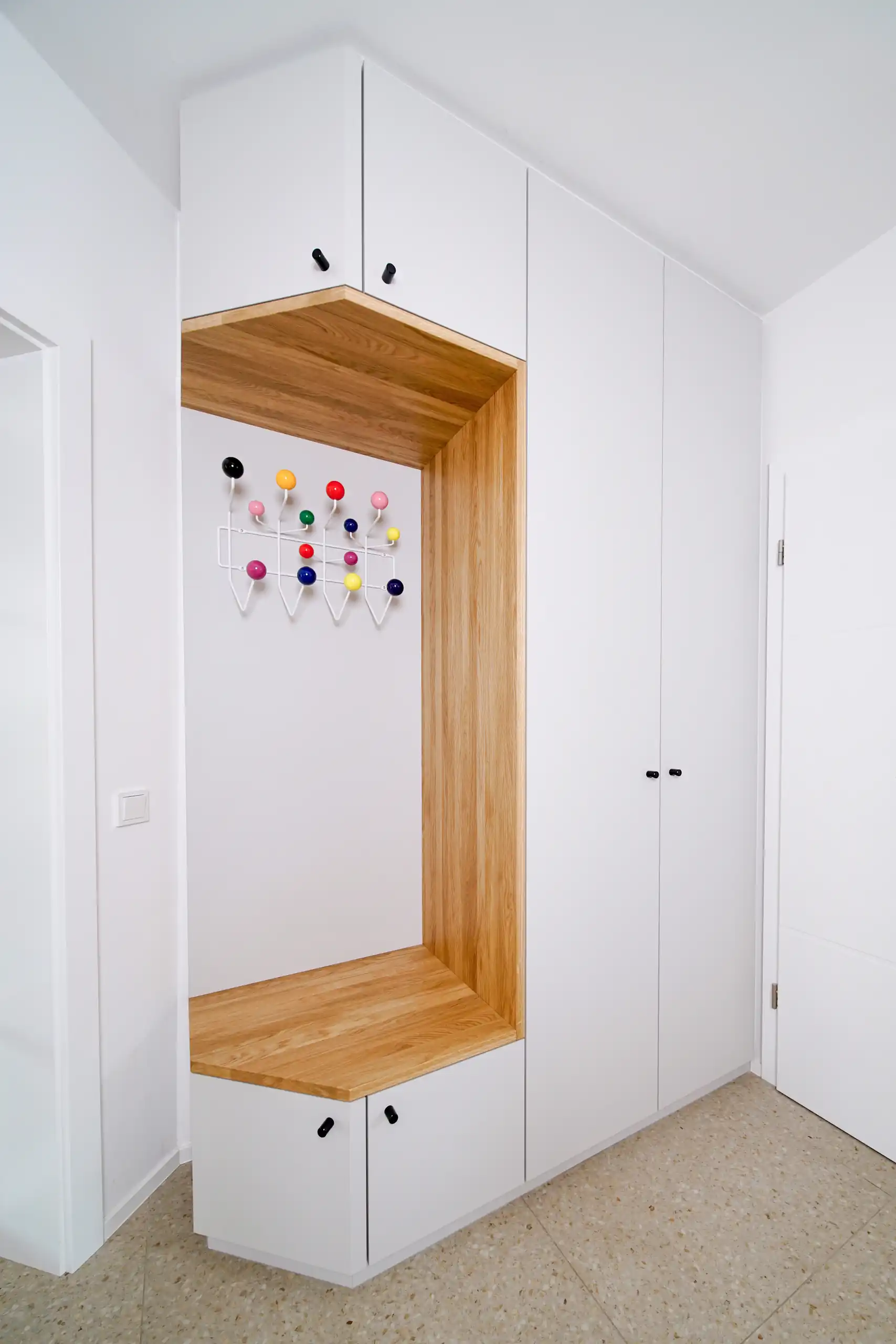 Maßgefertigte weiße Garderobe mit deckenhohen Schrankfronten, integrierter Eichenholz-Sitznische und farbiger Hakenleiste