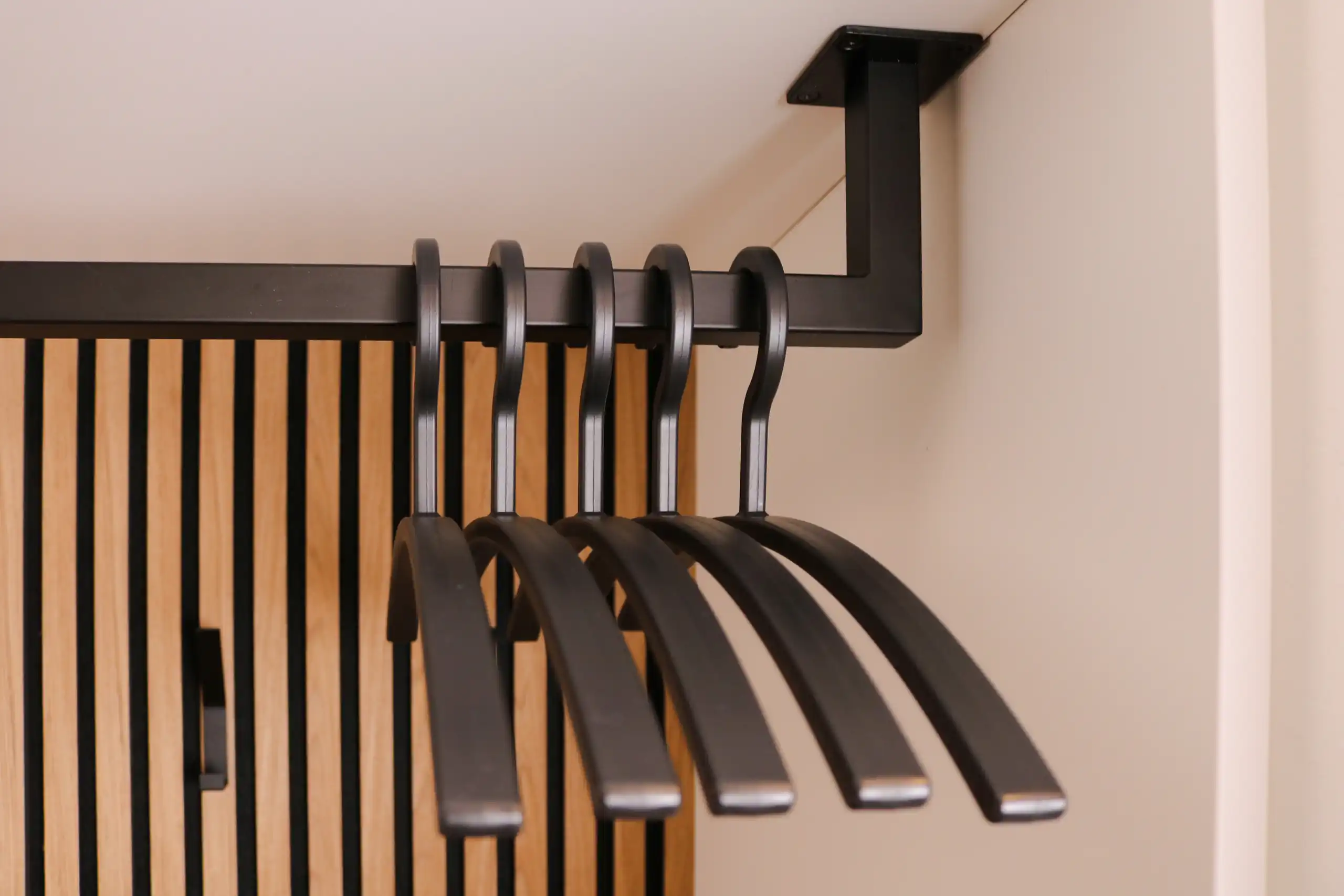 Ausziehbare schwarze Kleiderstange mit mehreren schwarzen Kleiderbügeln in einer maßgefertigten Garderobe