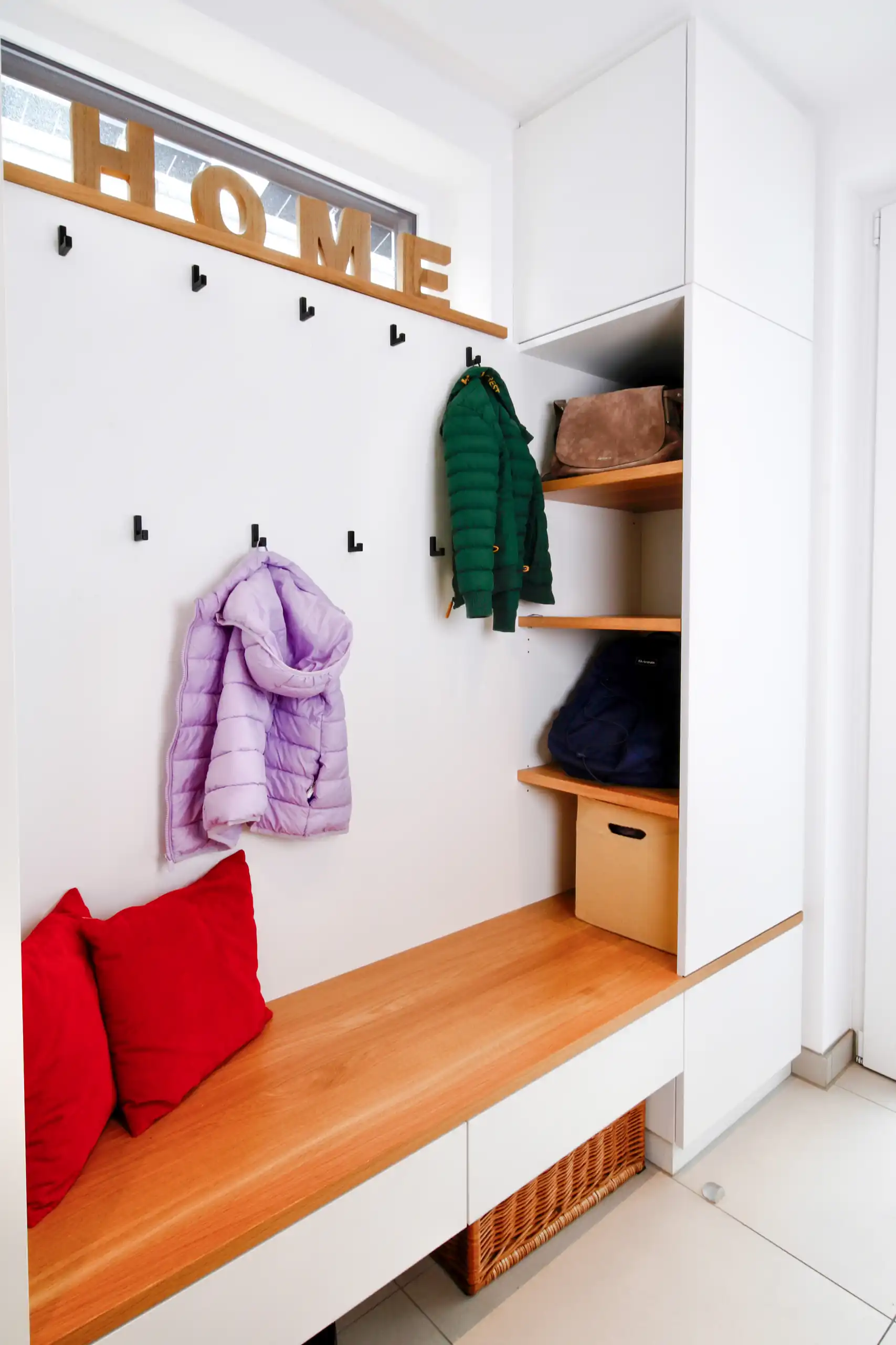 Helle Familiengarderobe mit Sitzbank aus Holz, Wandhaken für Kinderjacken, offenen Ablagen, hohen Schränken und Stauraumkörben unter der Bank