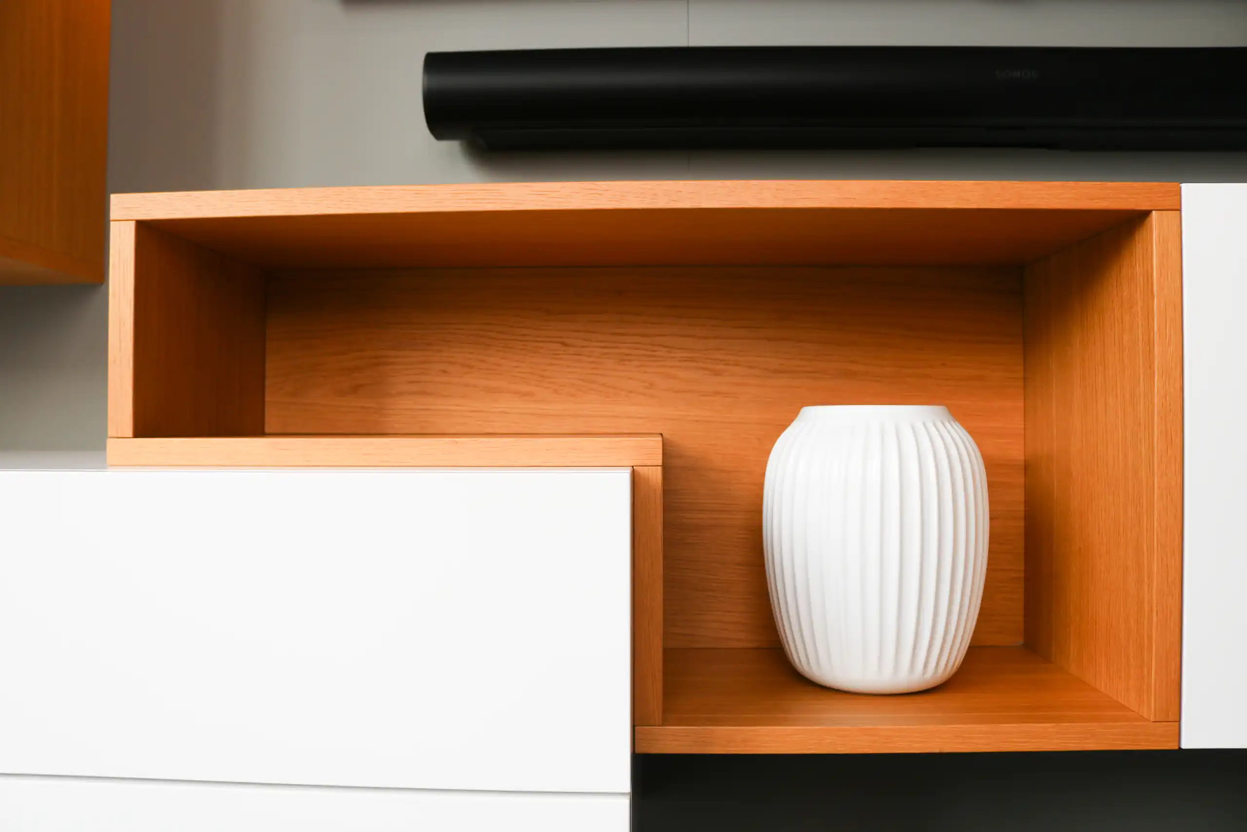 Offenes Regalfach aus Holz mit weißer Vase unter einer Soundbar