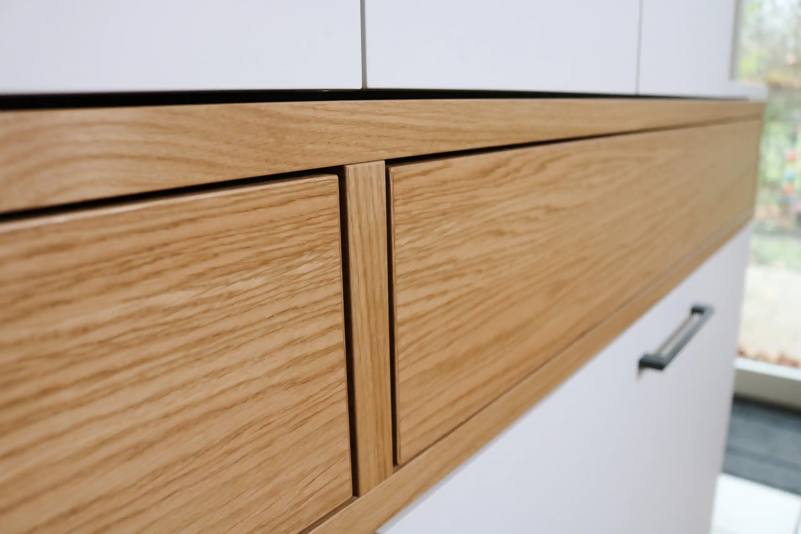 Detailansicht von Schubladenfronten aus Eichenholz mit sichtbarer Maserung in einem weißen Einbaumöbel